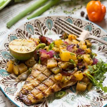 Close up of a dinner plate with a grilled barramundi fillet topped with fresh pineapple salsa.