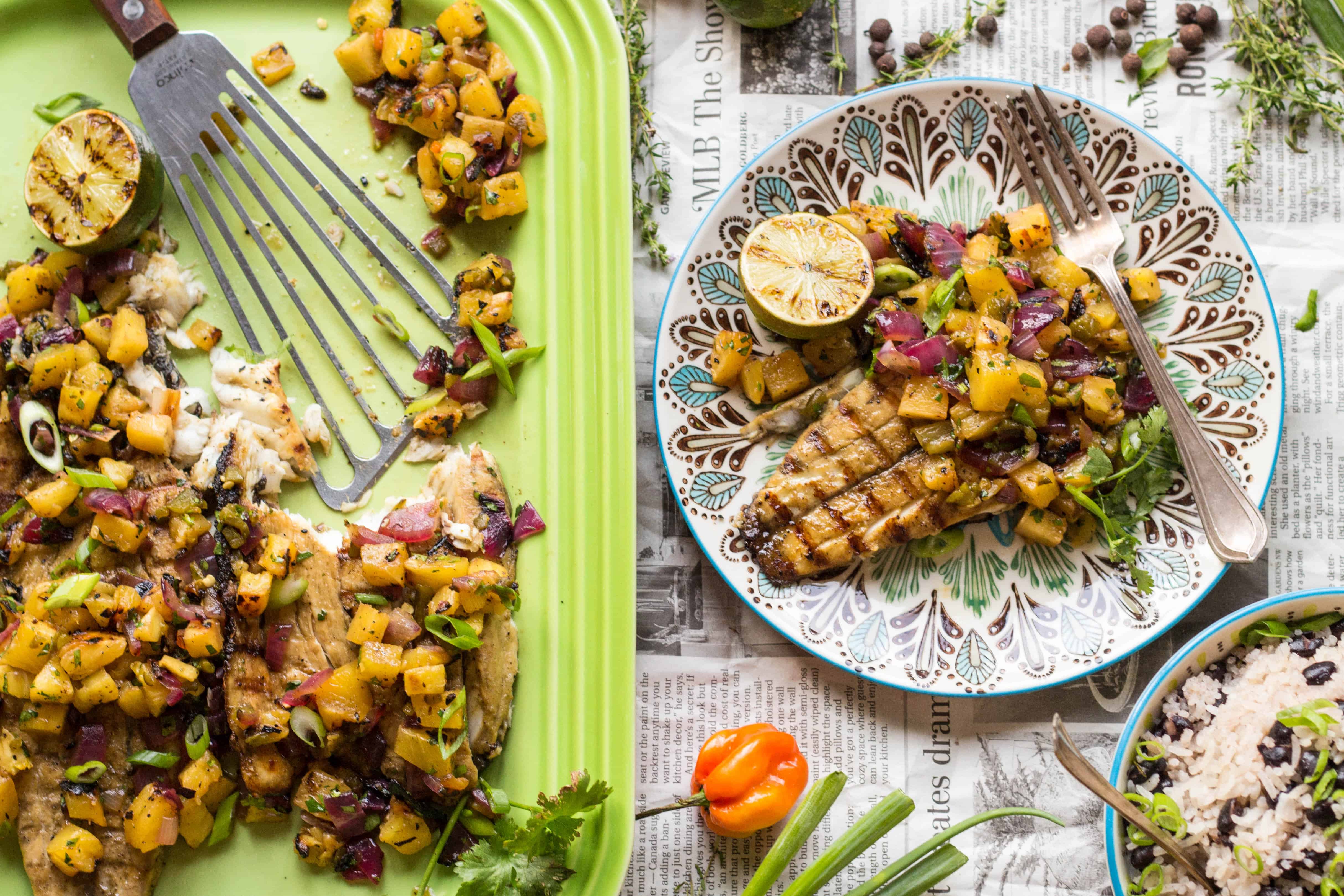A spatula on a green serving platter next to a dinner plate with barramundi and grilled pineapple salsa.