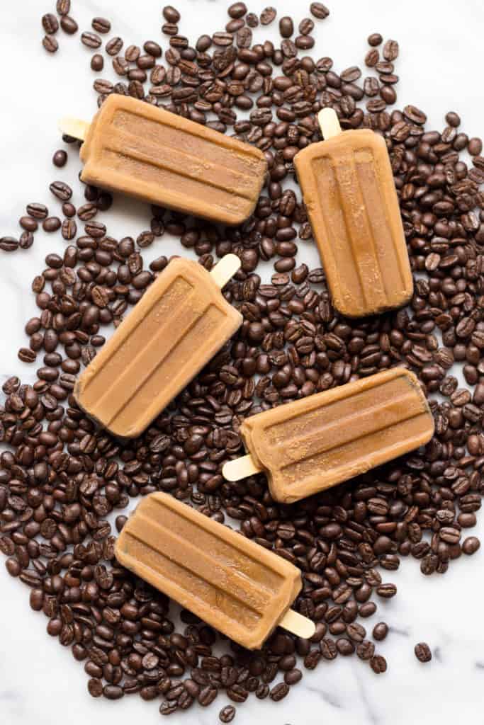 Vietnamese coffee popsicles nestled into fresh coffee beans on a table.
