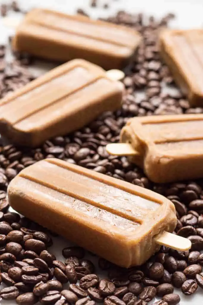 Close up of a coffee bean covered table with three Vietnamese coffee popsicles.