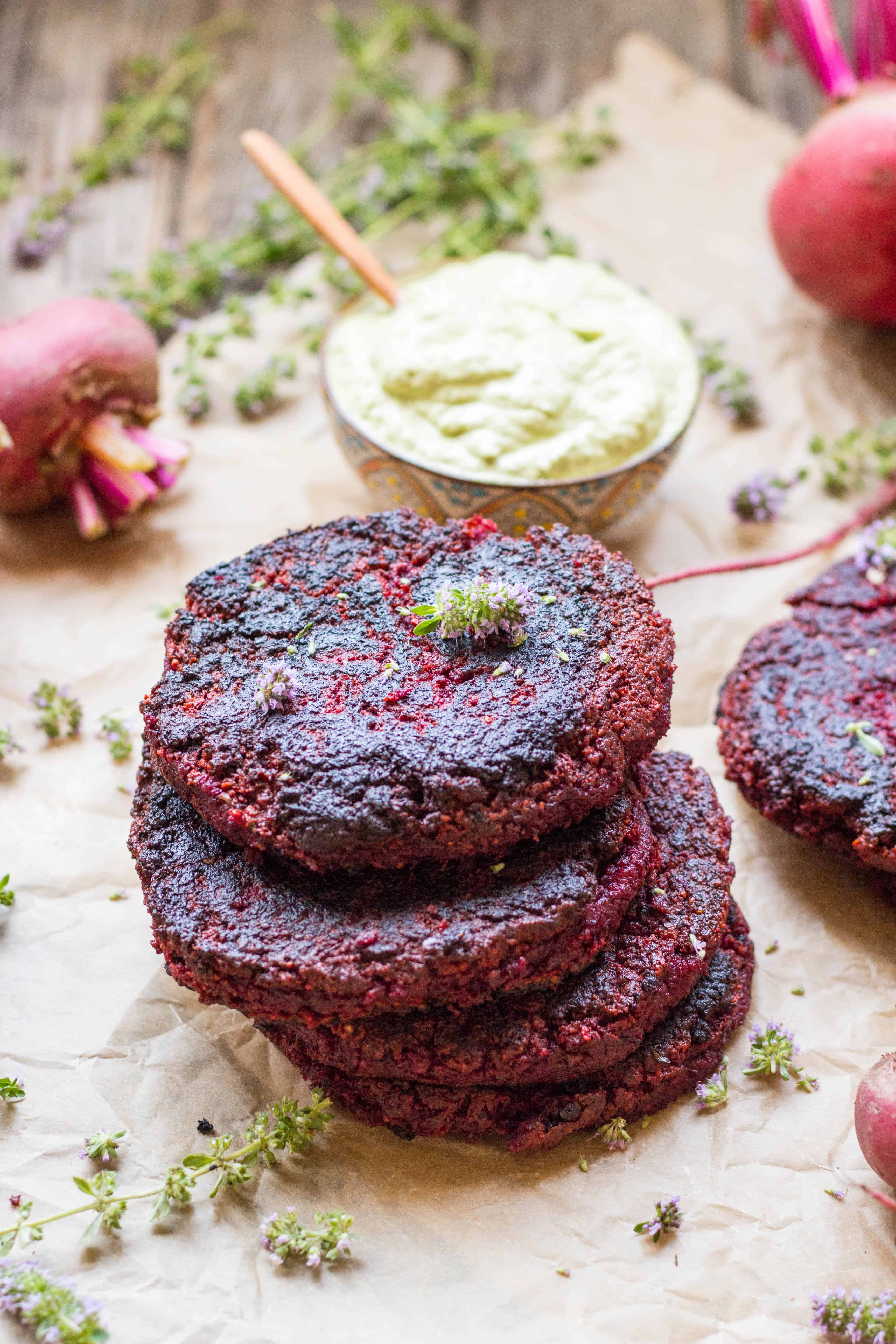 Close up of a stack of lentil beet burgers next to a small bowl of green goddess dessing.