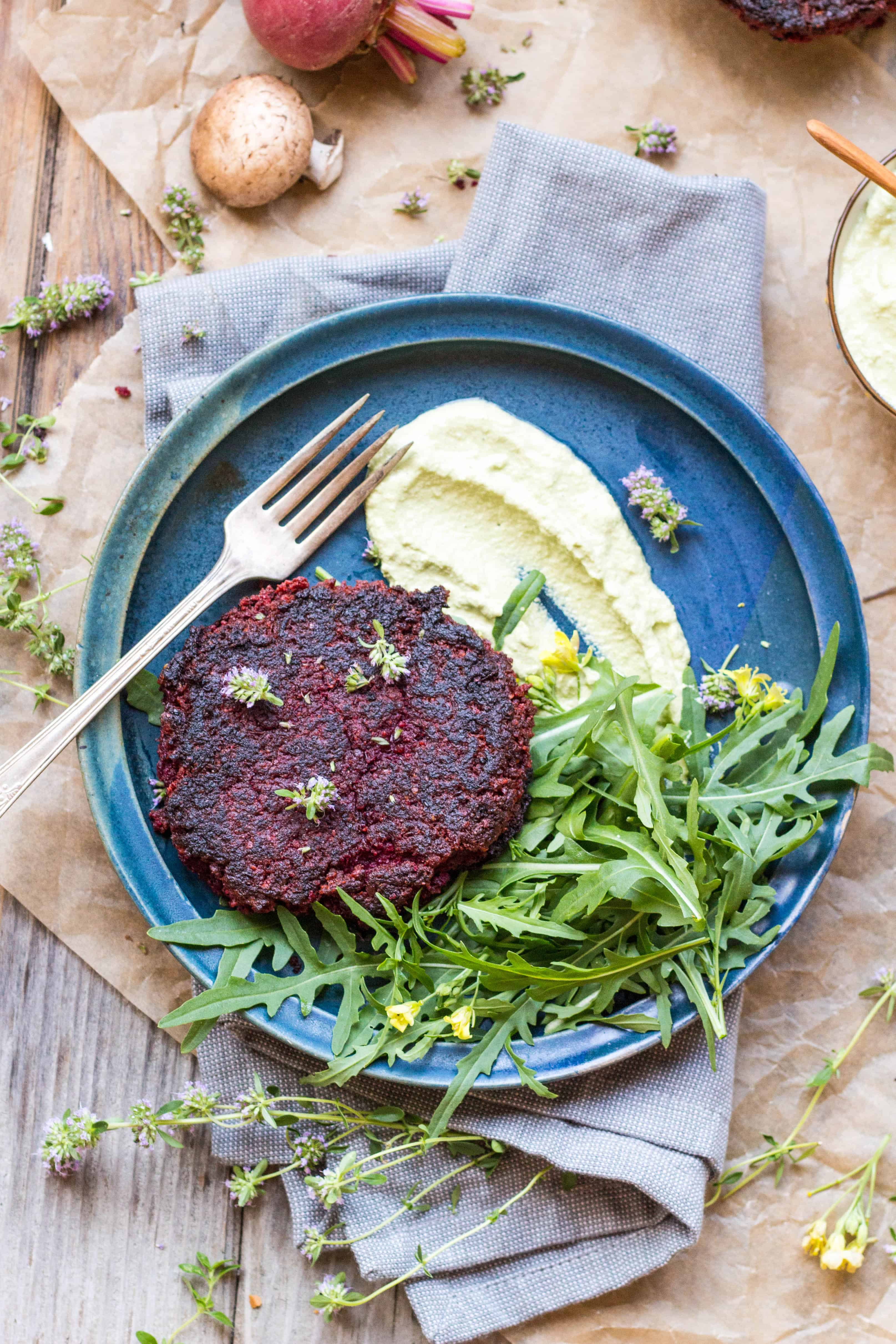 A blue plate with green goddess dressing, lentil beet burger, and side green salad next to a fork.