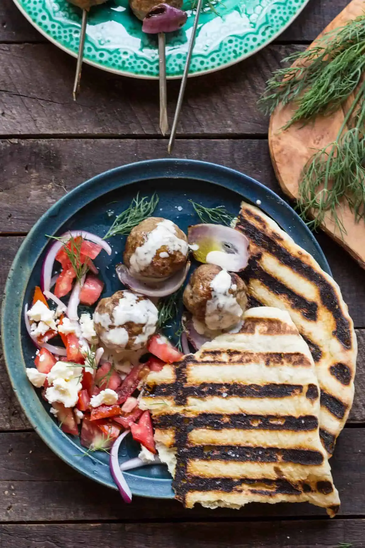 A large blue dinner plate with grilled pita, lamb meatballs, and tahini.