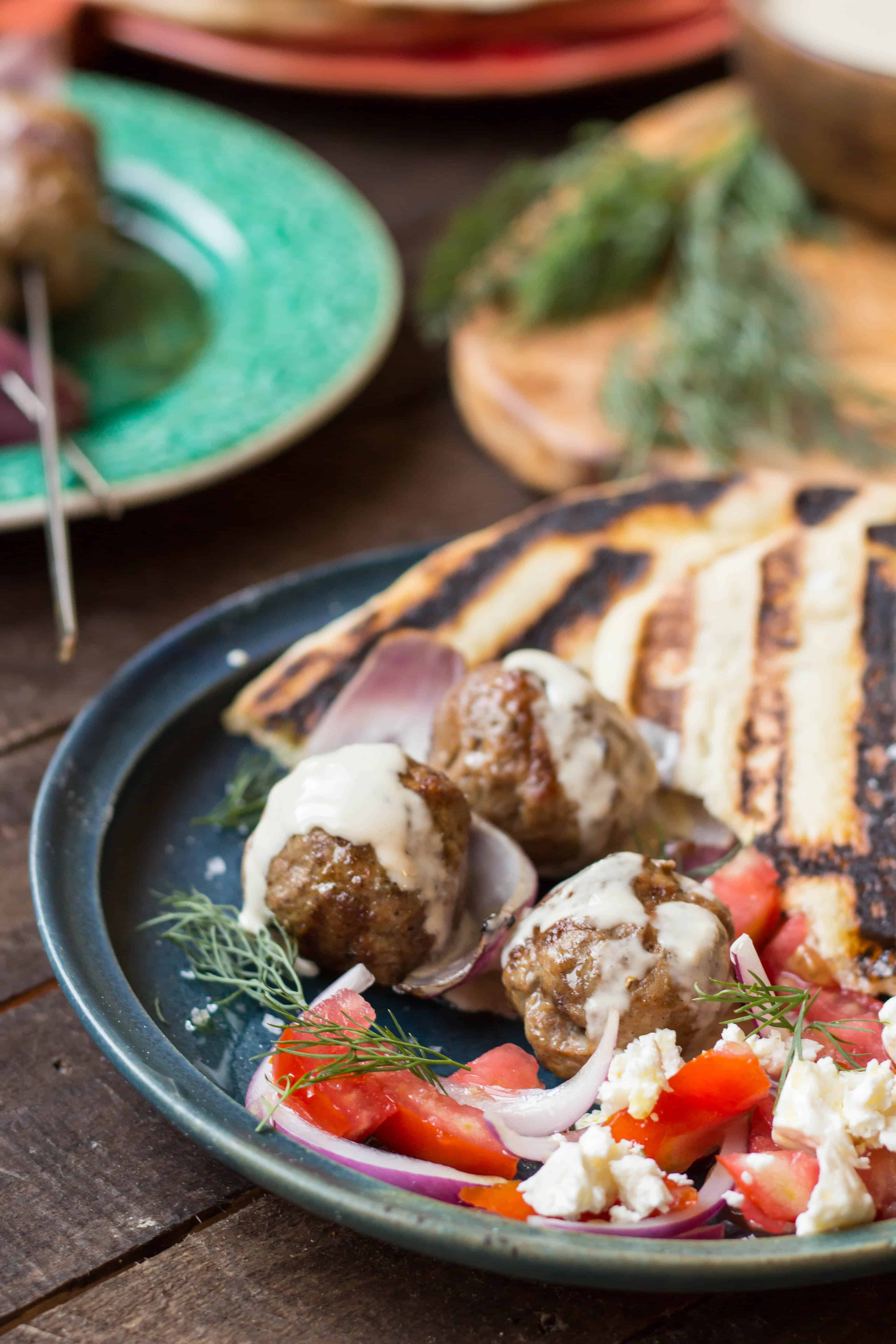 Close up of grilled lamb meatballs and red onion drizzled with tahini sauce.
