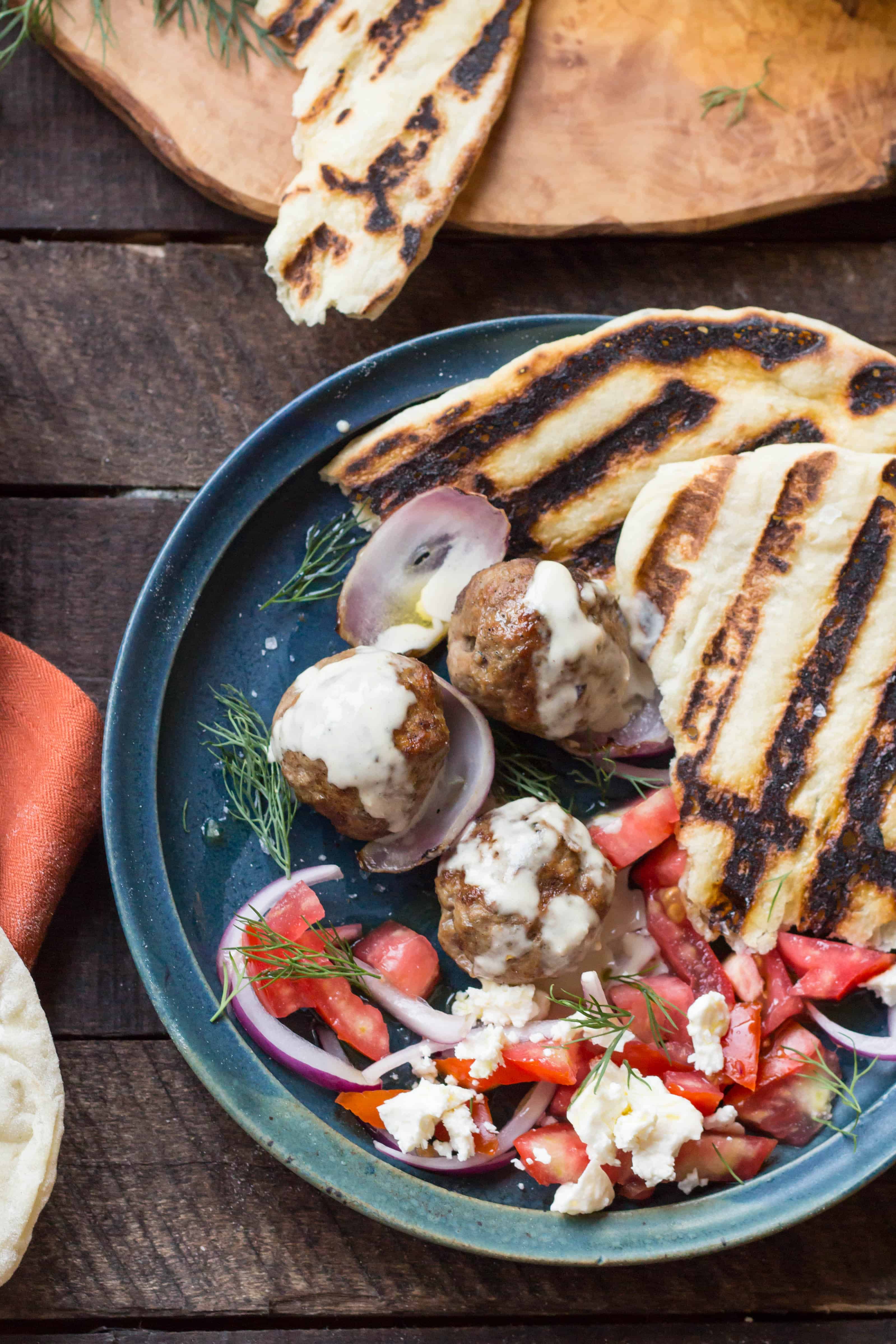 Top view of a blue dinner plate with grilled pita, lamb meatballs, and tomato salad.