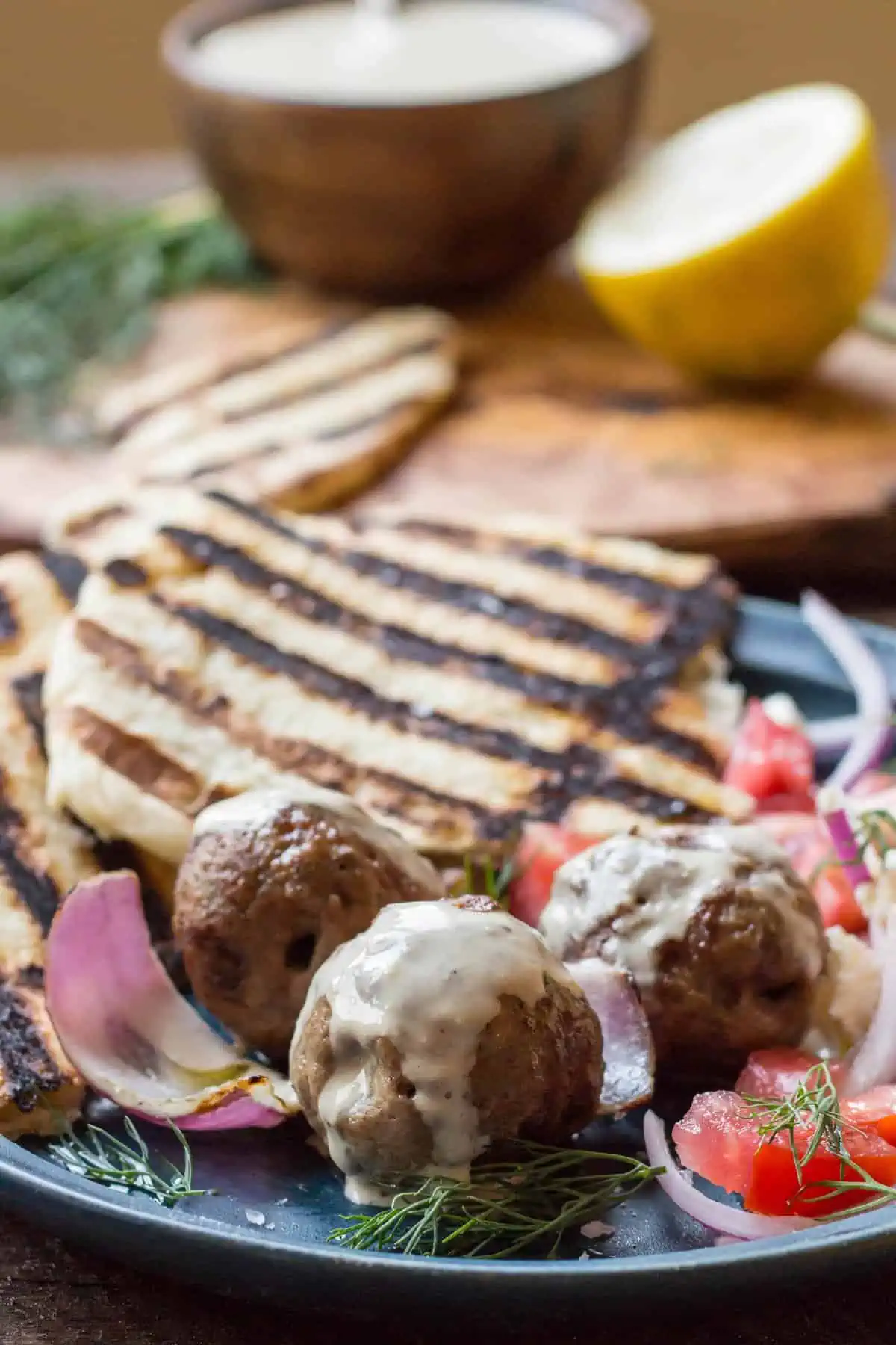 Close up of lamb meatballs drizzled with tahini and grilled pita in the background.