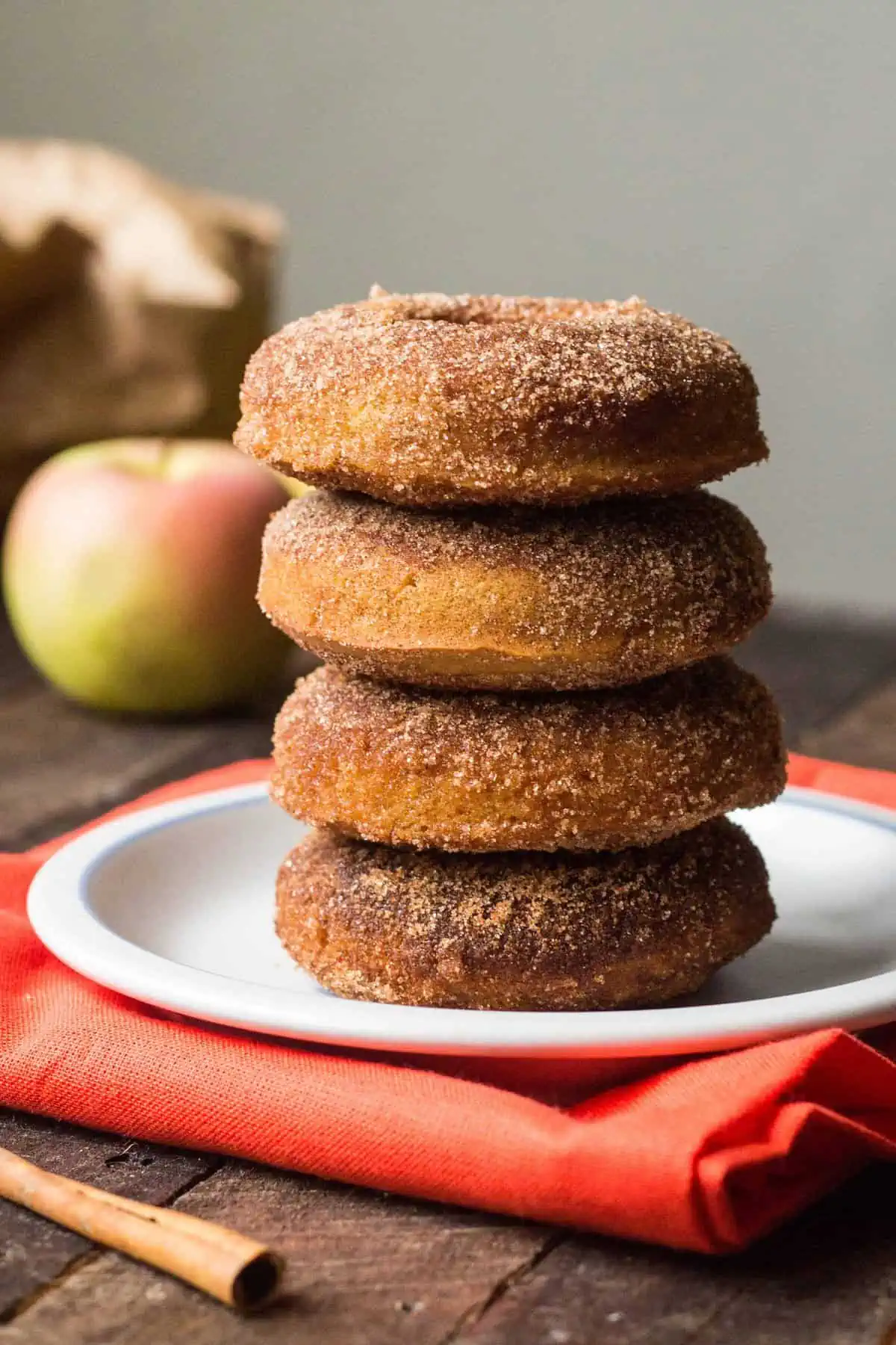 Stack of four baked apple cider doughnuts covered in cinnamon sugar.