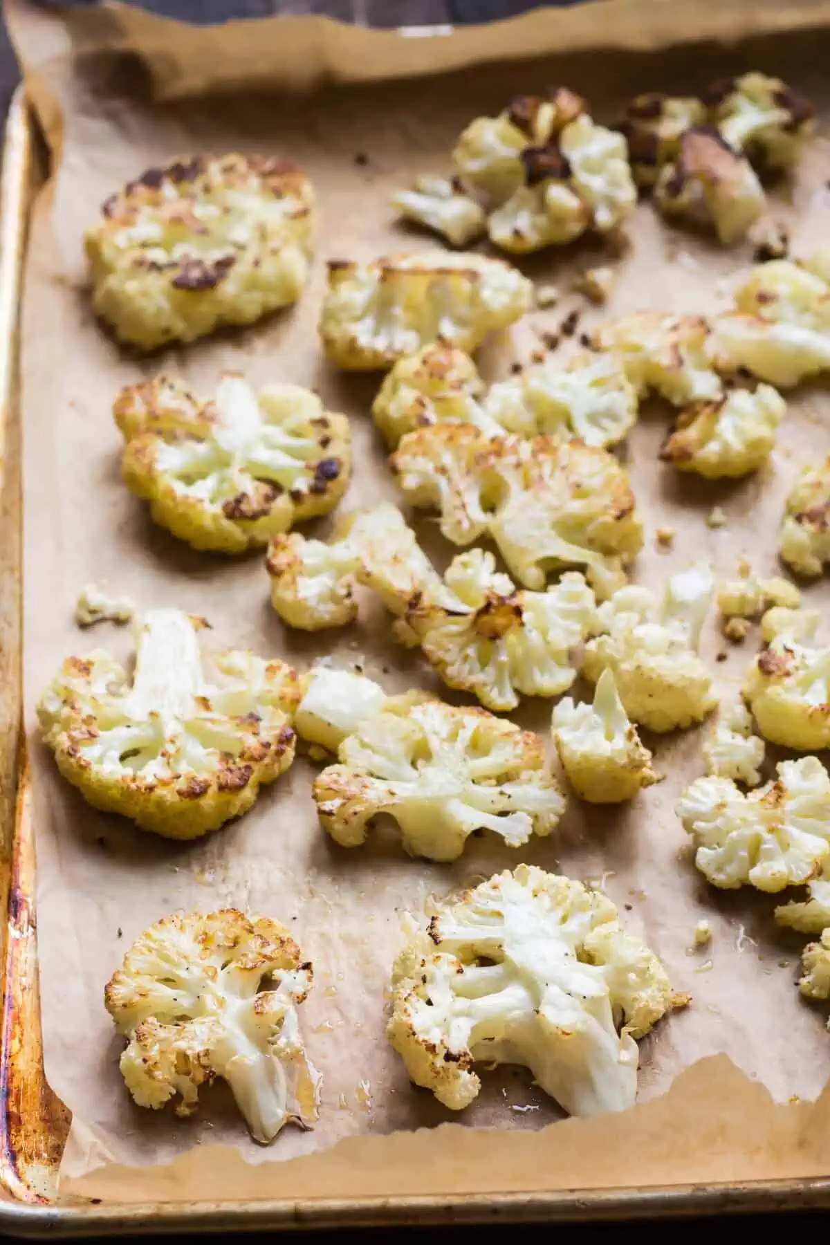 Roasted cauliflower florets on a parchment lined baking sheet.