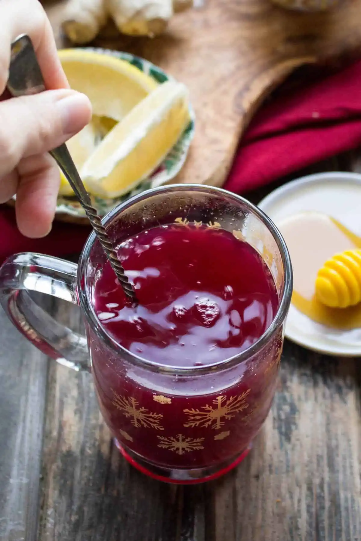 A hand stirring a spoon in a clear mug of blueberry ginger hot toddy.