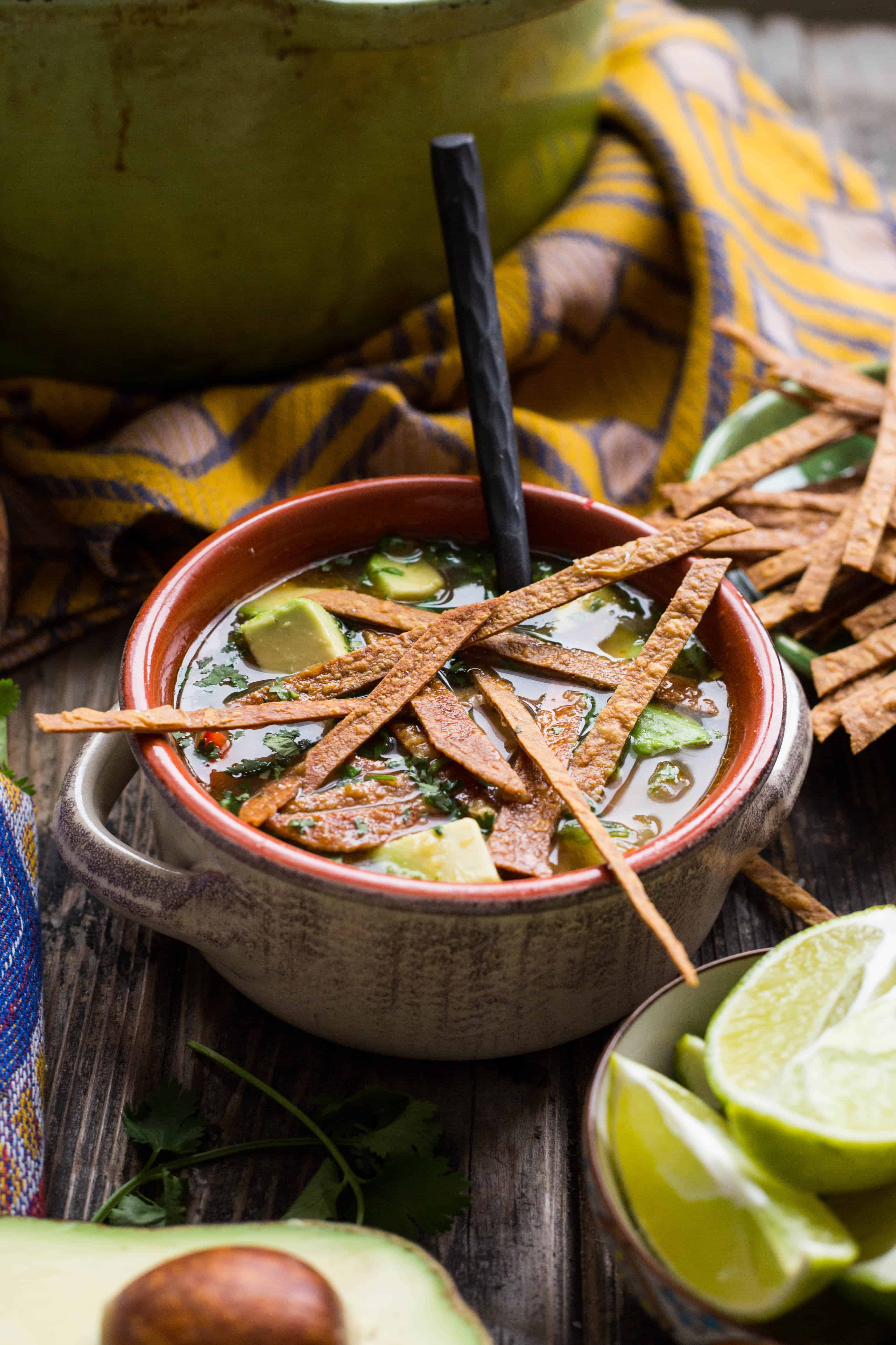 A bowl of chicken tortilla soup with avocado and a spoon.