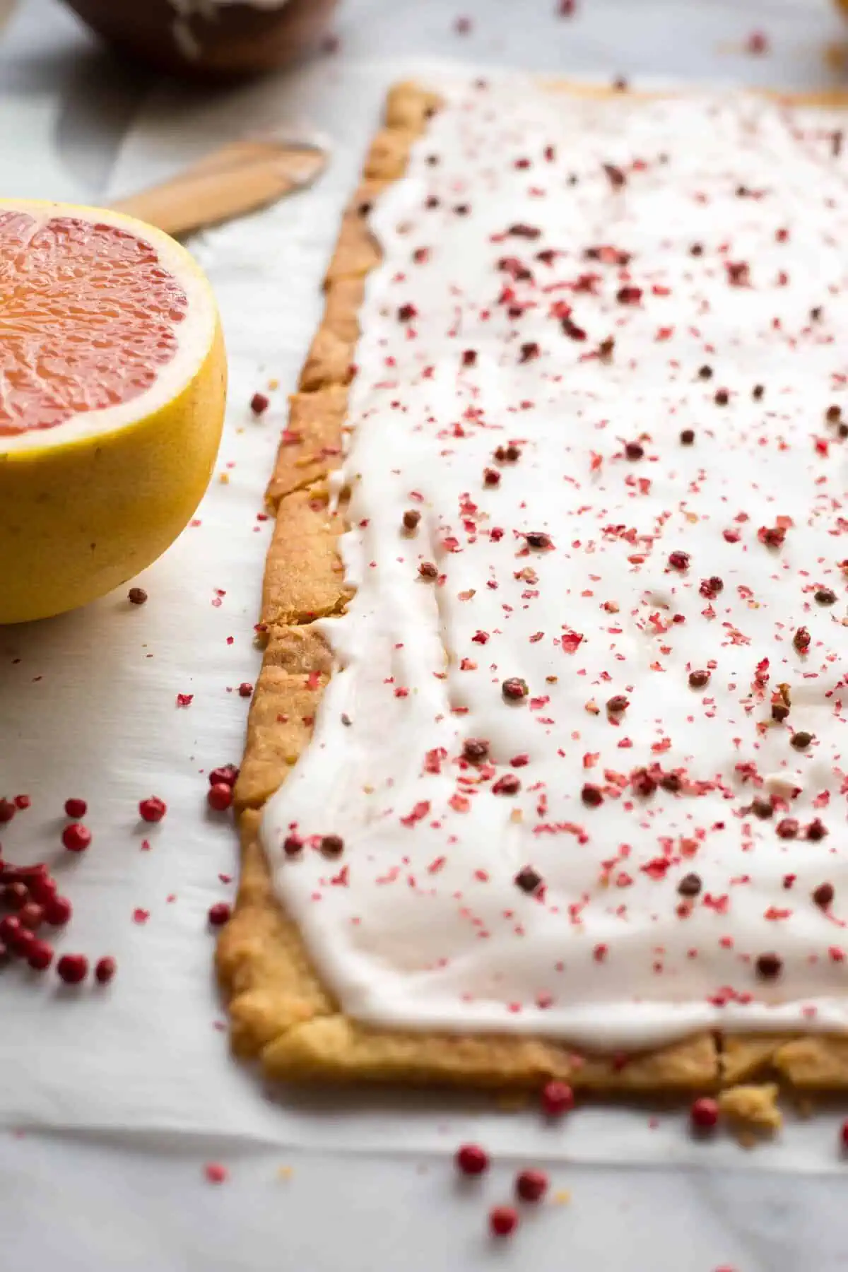 Close up of grapefruit shortbread that are iced and have pink peppercorns on top.