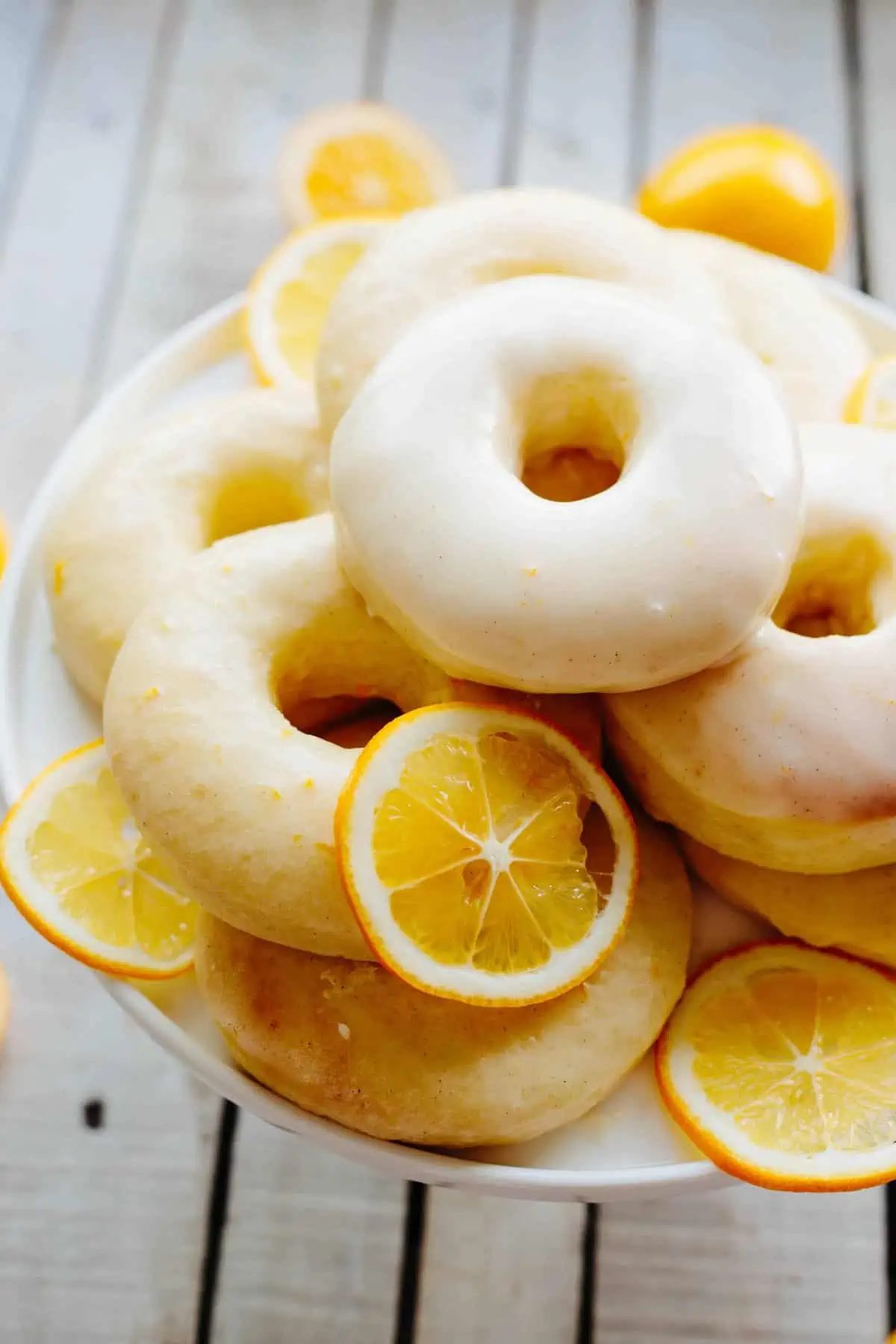 Close up view of iced lemon doughnuts and thin slices of lemon on a white cake stand.