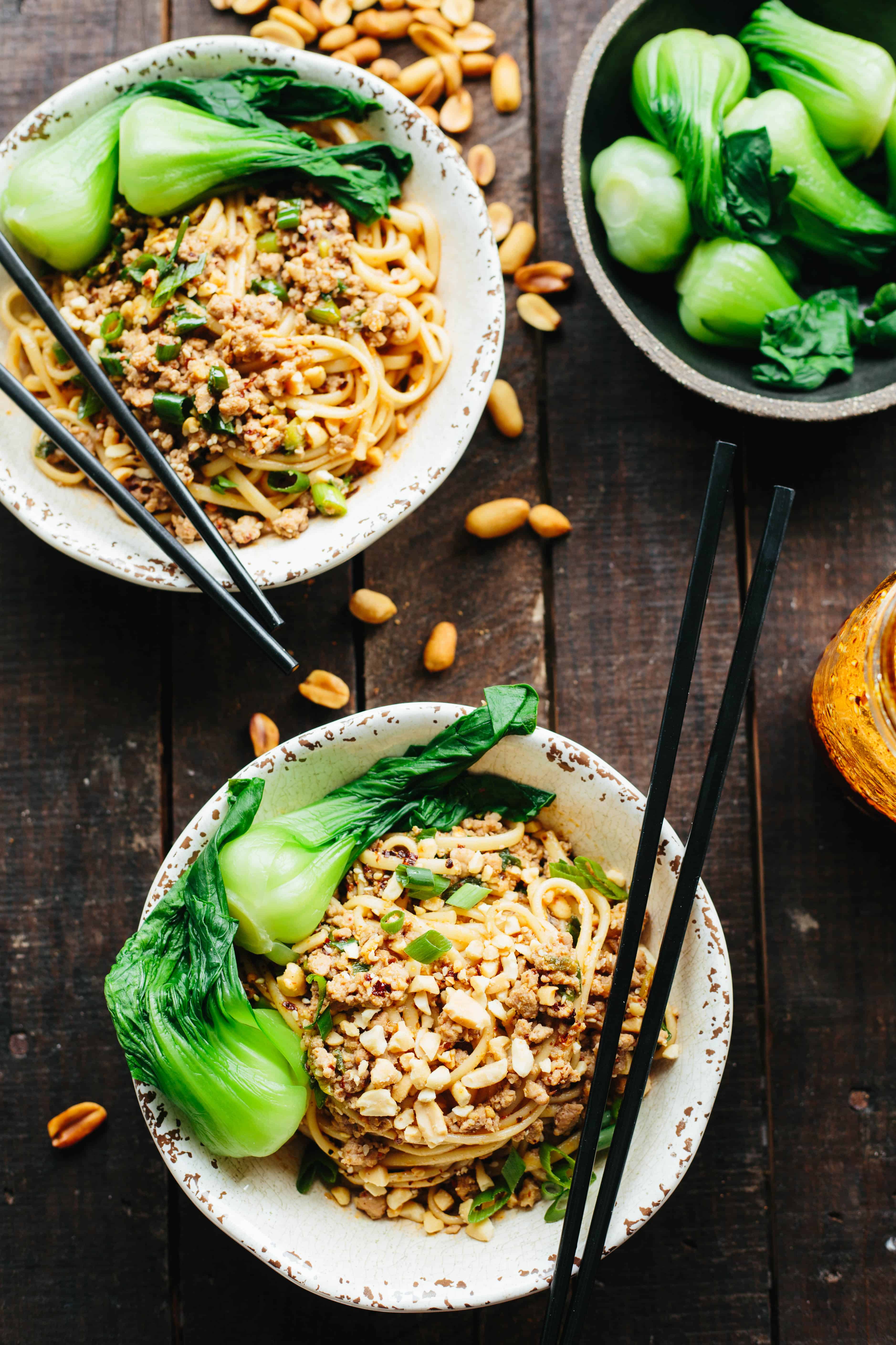Baby bok choy and dan dan noodles with chopsticks stuck in them in white bowls.