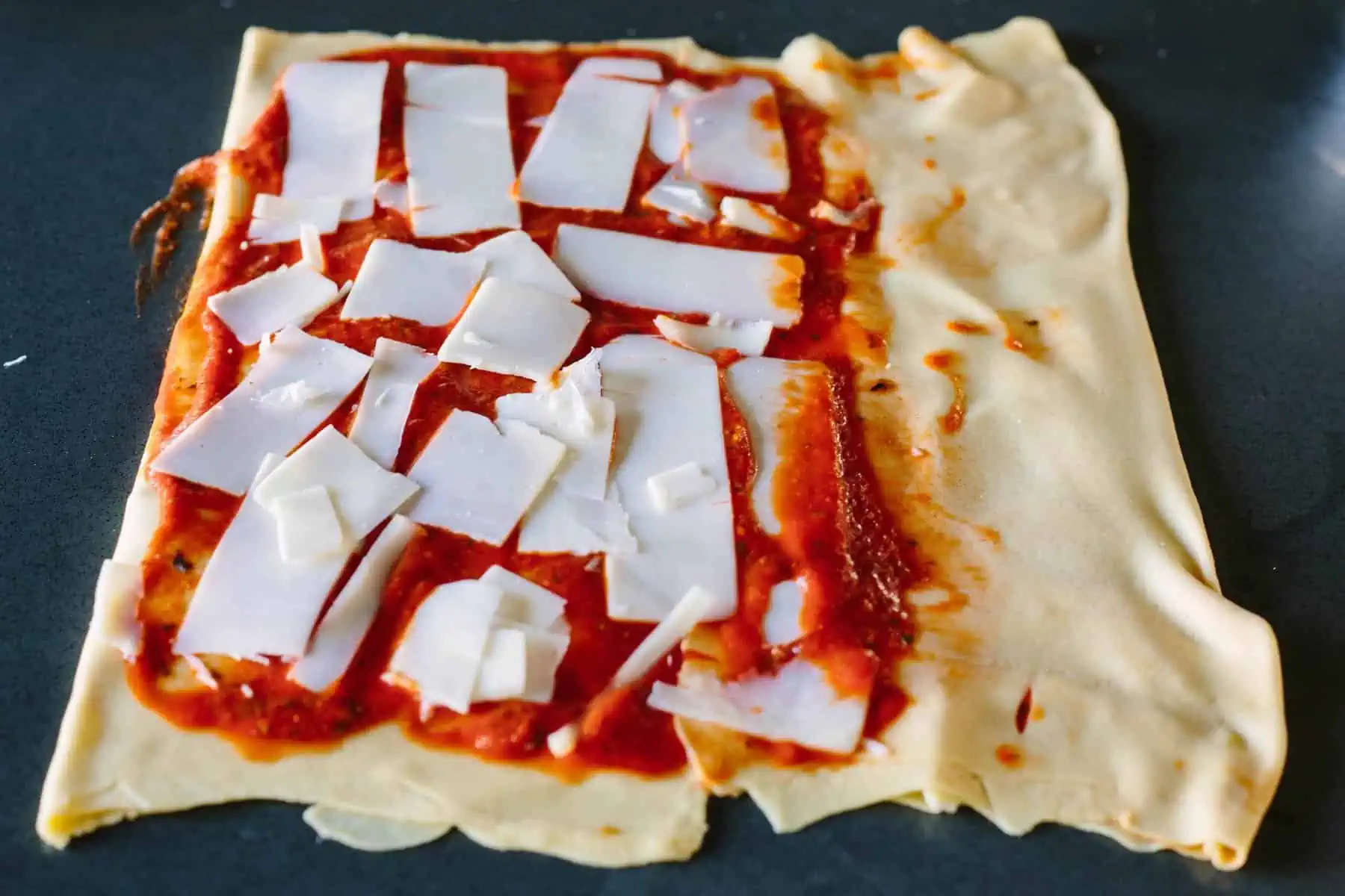Folding bread dough over layers of cheese and pizza sauce.