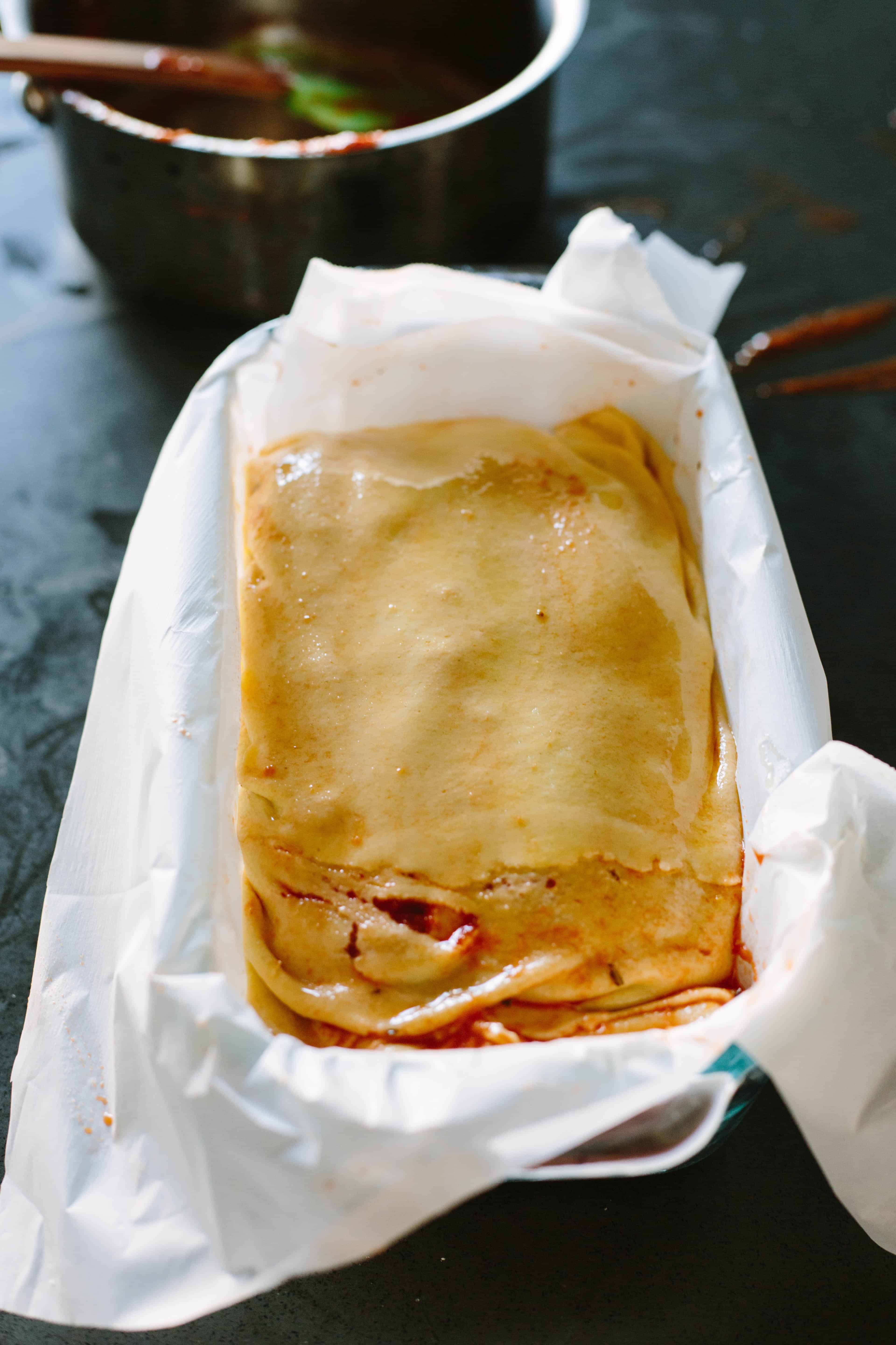 Folded pizza babka dough placed into a parchment lined loaf pan.