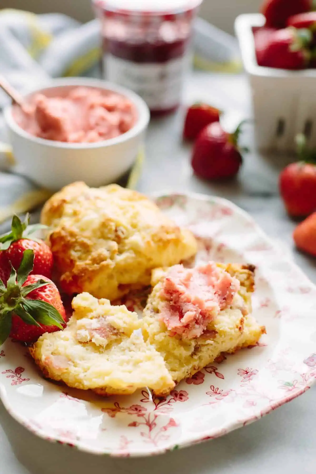 A whole scone and one split open and spread with butter on a small plate with whole strawberries.
