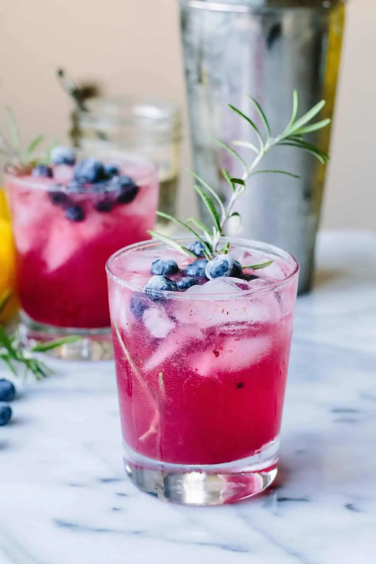 Close up of a glass of bluberry vodka spritzer with fresh blueberries and a sprig of rosemary.