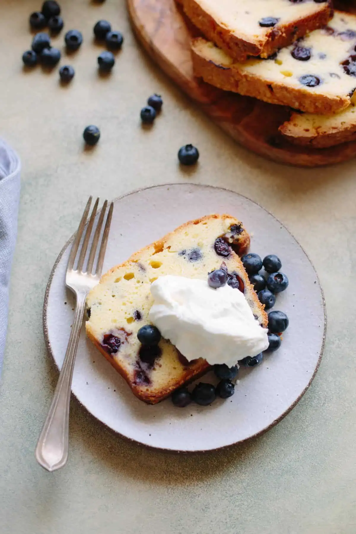 A slice of lemon blueberry pound cake topped with whipped cream on a dessert plate.