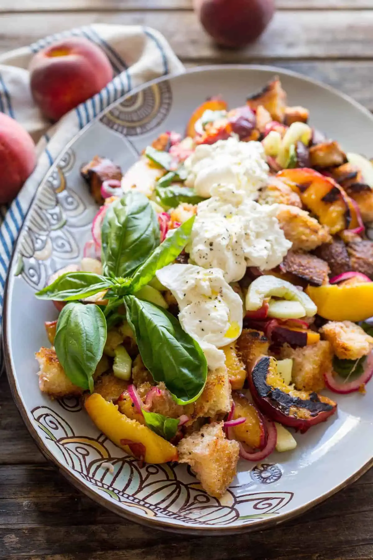 Top view of grilled peach panzanella topped with fresh basil and burrata.