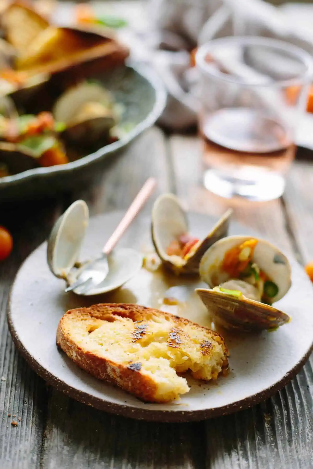 Toasted, buttered baguette and tomato topped clams on a white dinner plate.