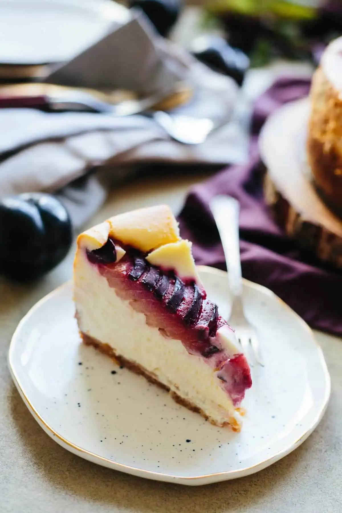 Angled shot of a slice of plum ricotta cheesecake and a fork on a white dessert plate.