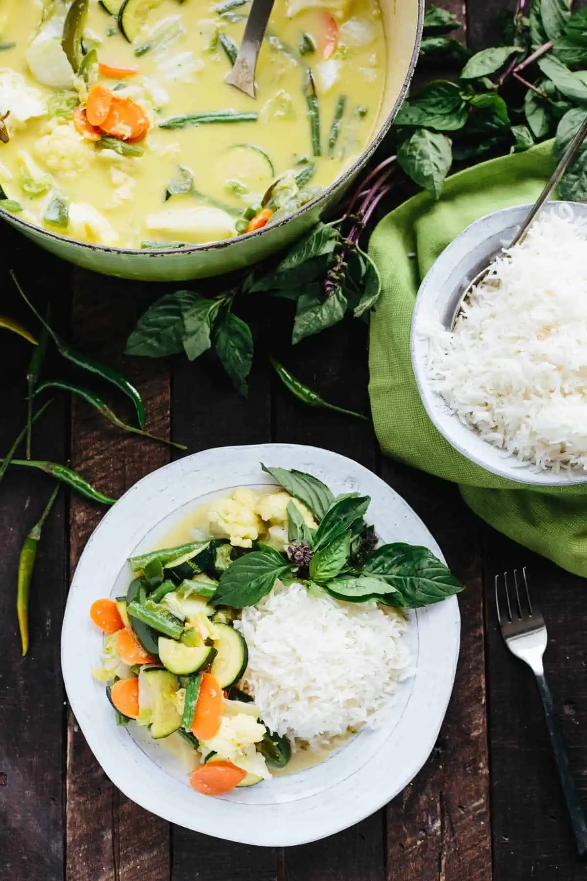 A table set with a large pot of curry, a bowl of rice, and a large helping of both on a white dinner plate.