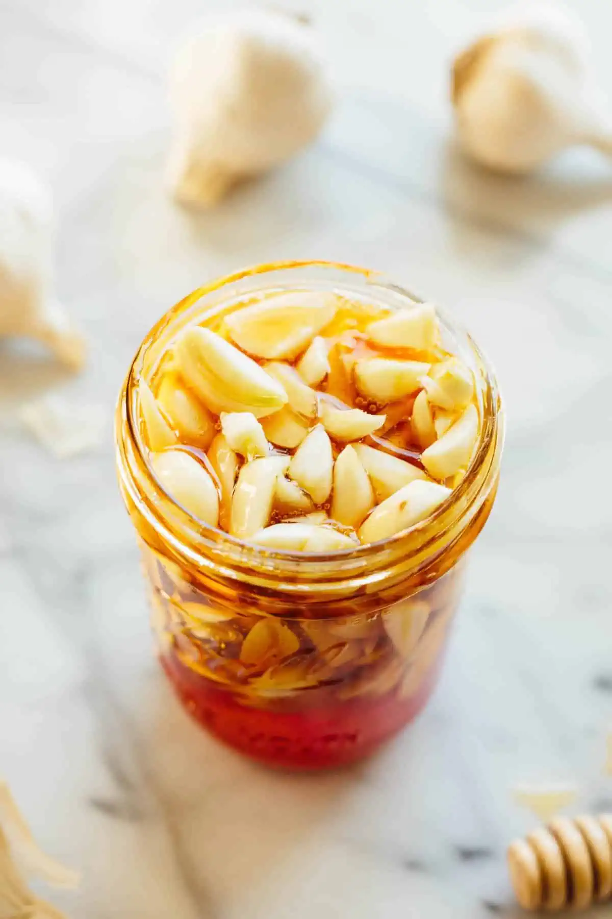 Glass jar of honey with peeled garlic cloves tucked into the top.