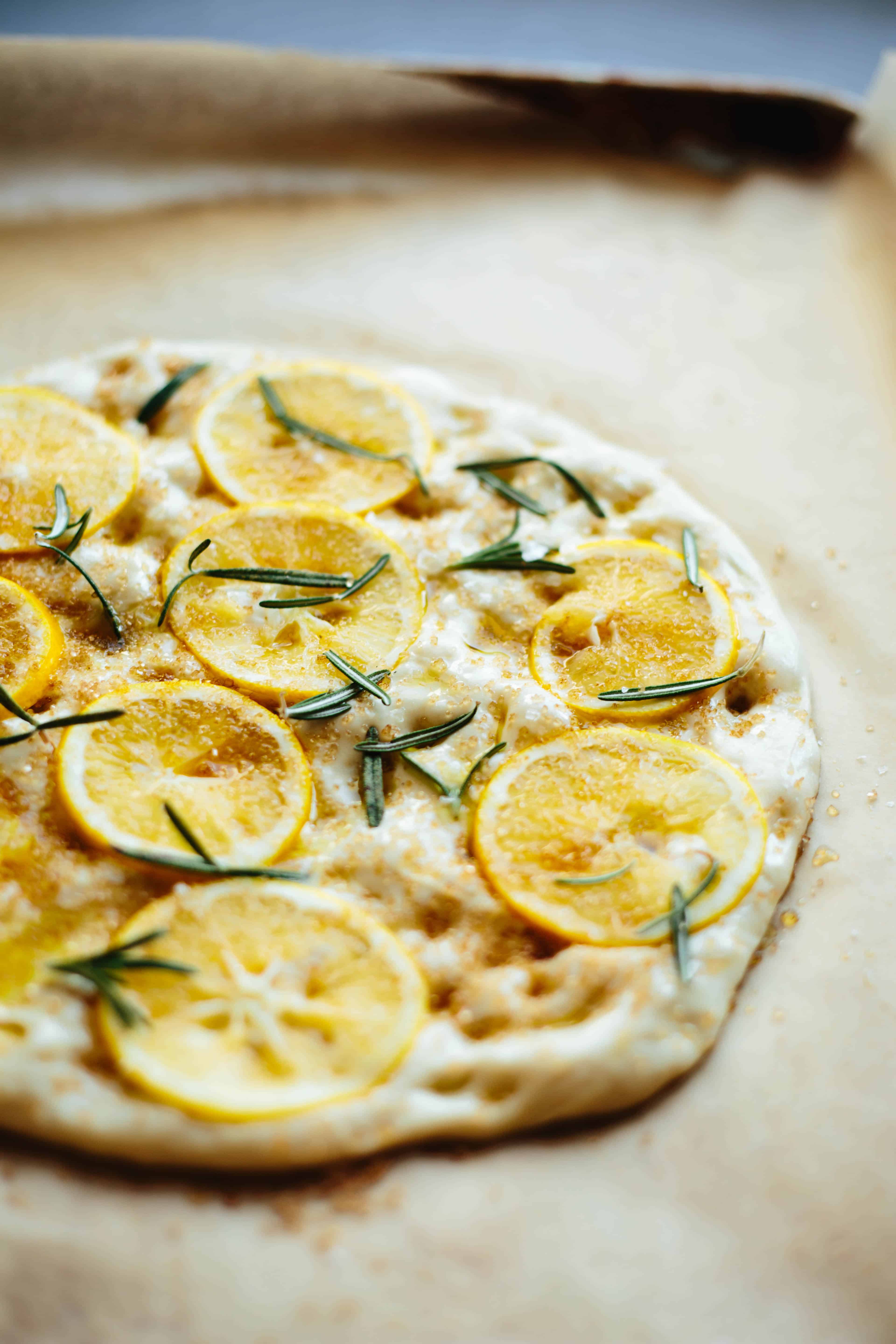 A round focaccia dough with lemon slices and herbs pressed into the top.