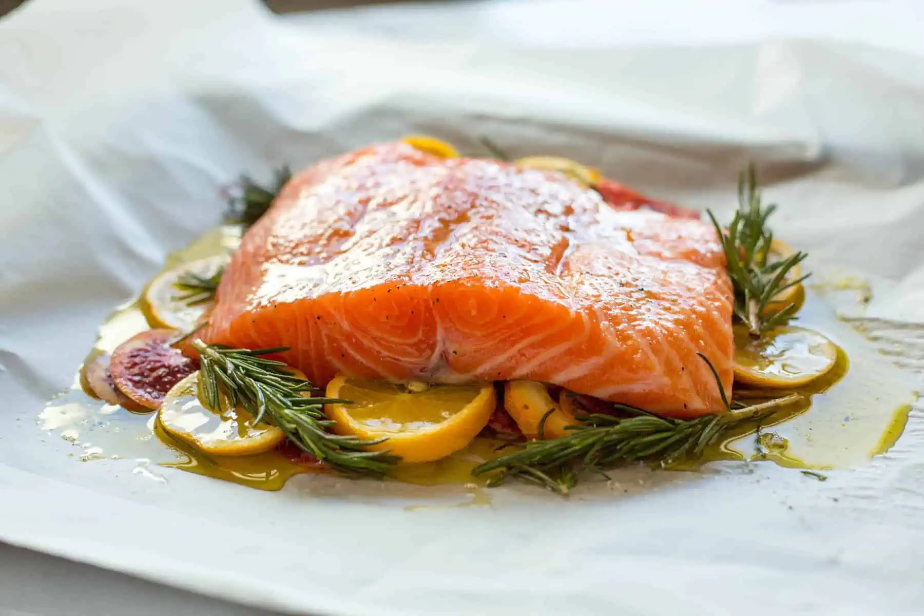A salmon fillet on a bed of citrus and herbs ready to be wrapped in a parchment pocket.