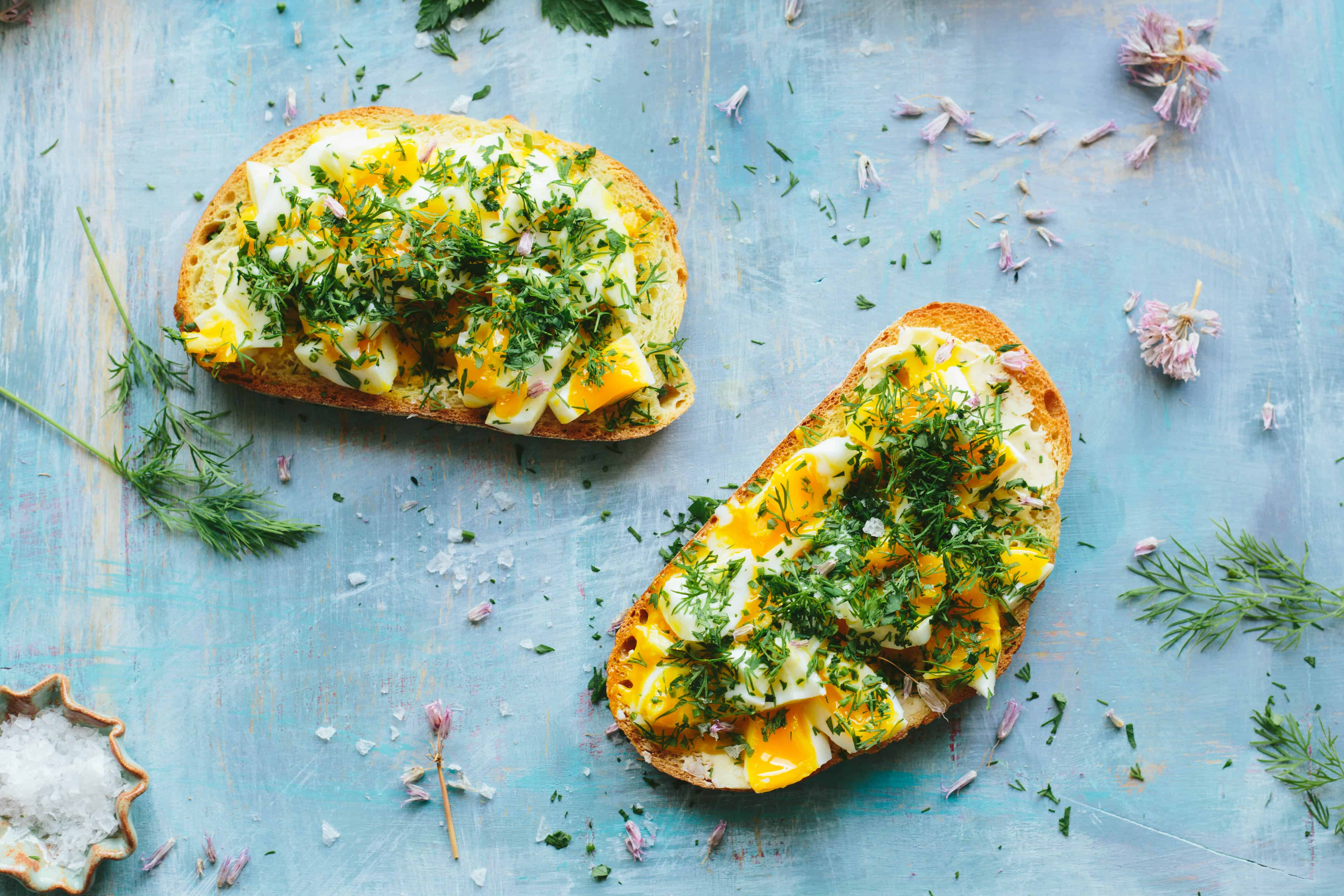 Top view of two slices of toast topped with smashed boiled eggs and chopped fresh herbs.