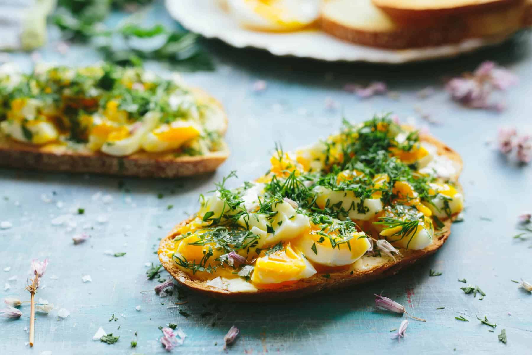 Close up of a slice of toasted baguette with smashed eggs and fresh herbs.