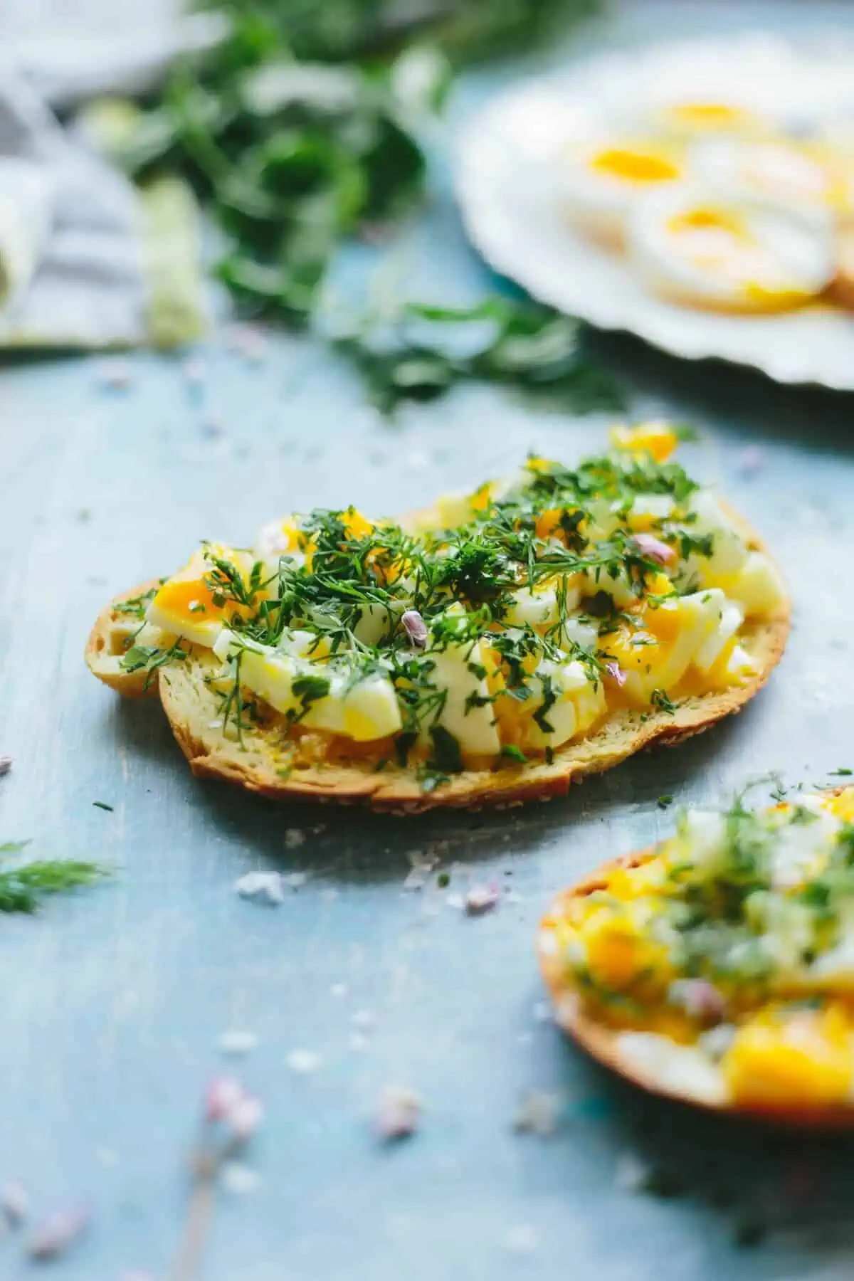 Slice of toast with smashed soft boiled eggs topped with sprinkled fresh herbs.