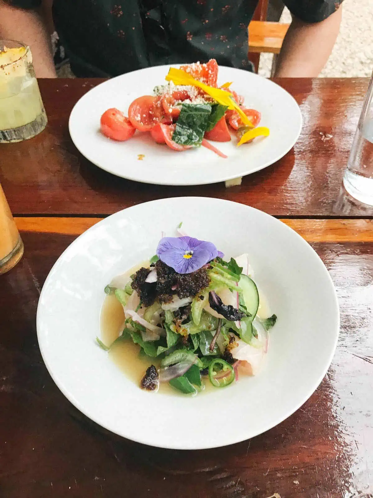 Two small plates of salad at a restaurant\'s shiny wood table.