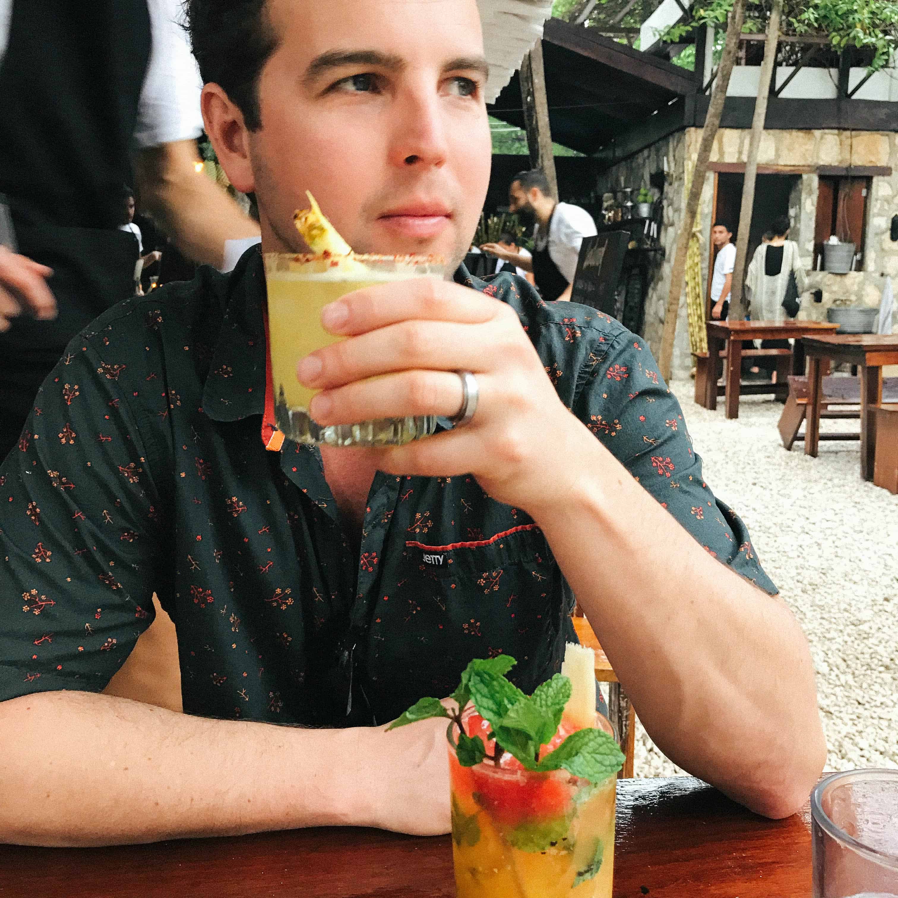 A man having a cocktail outside at a restaurant table.