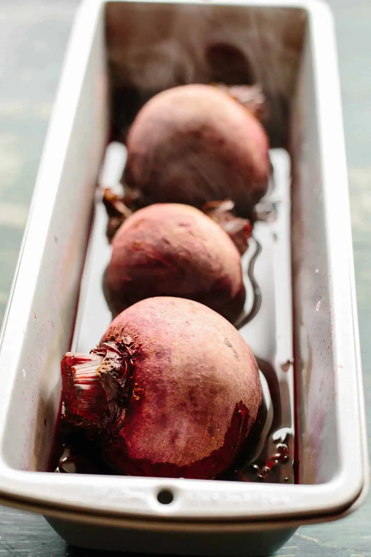 Three roasted beets sitting in a baking dish.
