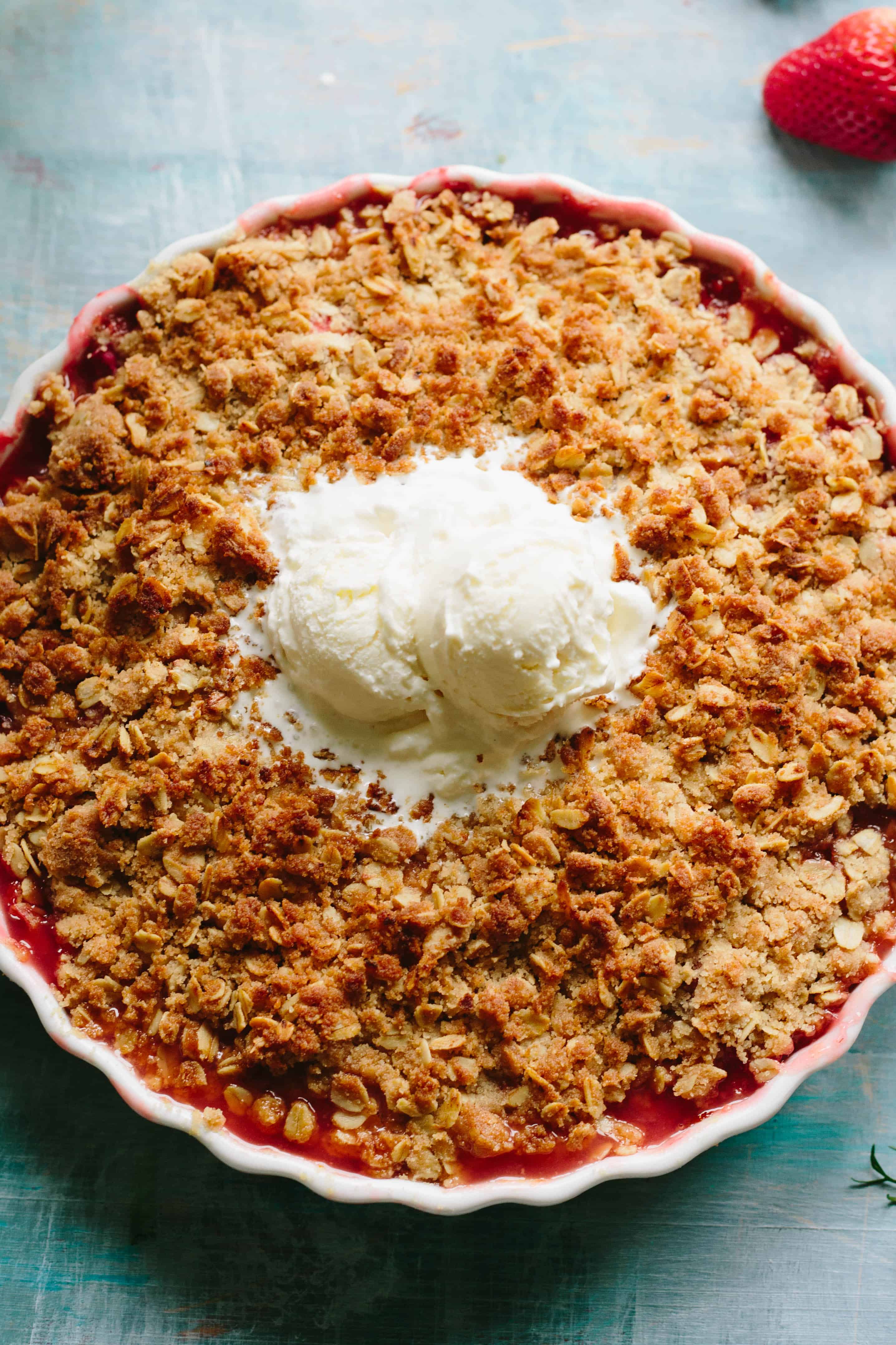 Two scoops of vanilla ice cream melting into the top of a strawberry rhubarb with apricot crisp.