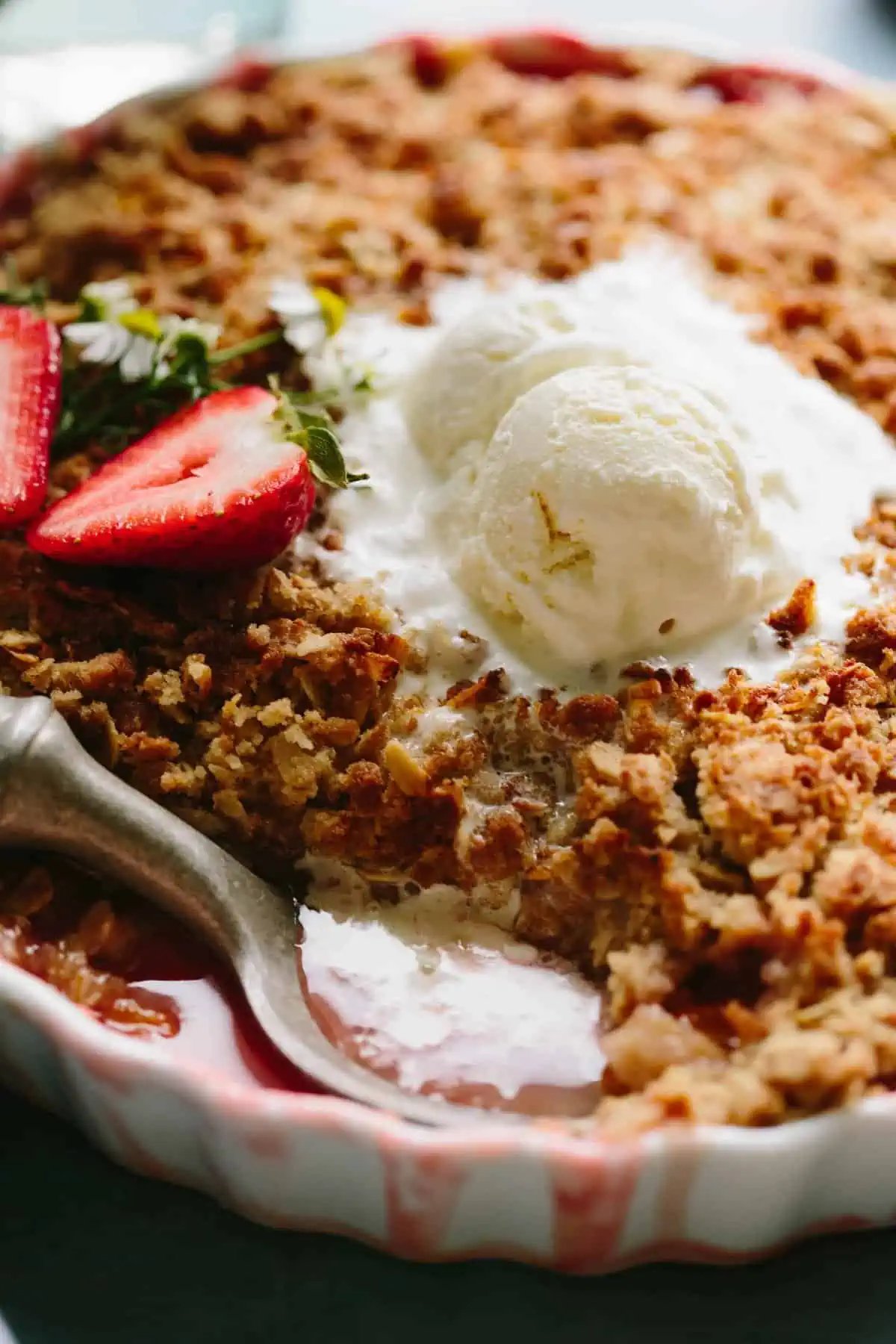 Close up view of a scoop of vanilla ice cream melting over strawberry crisp.