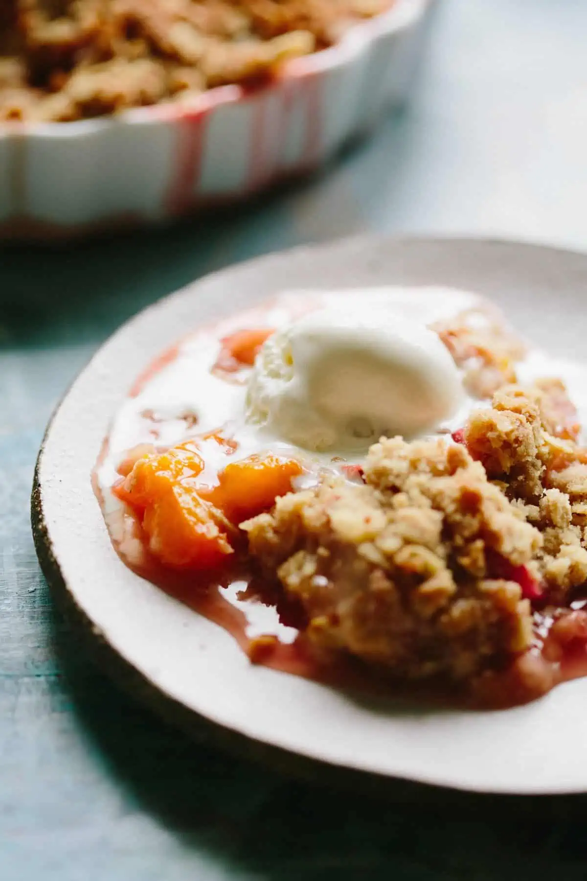 Close up shot of a dessert plate filled with warm apricot strawberry rhubarb crisp and melting vanilla ice cream.