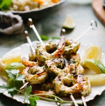 Grilled shrimp on metal skewers on a plate with lemon wedges.
