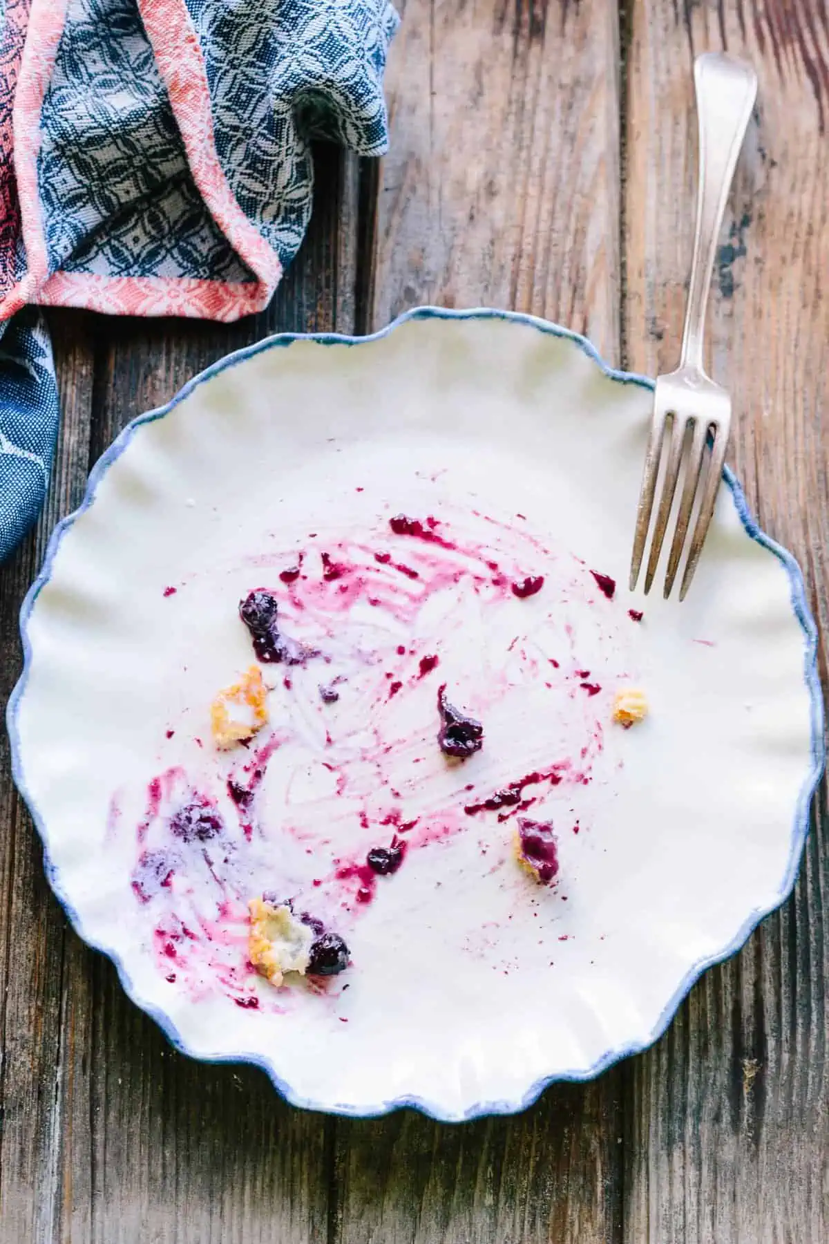 An empty dessert plate with streaks of blueberry pie filling.