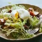 Close up of a dinner plate with lyonnaise salad.