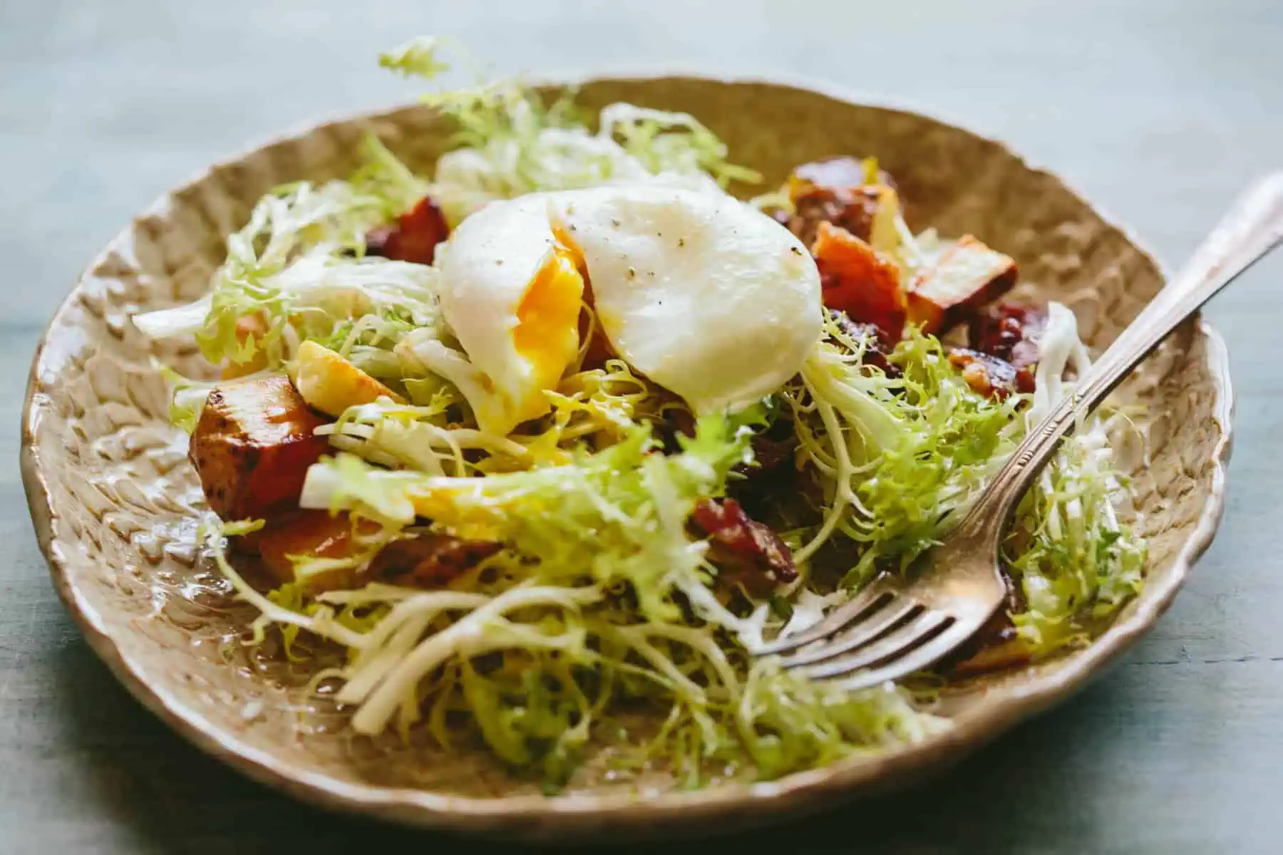 Tan luncheon plate with lyonnaise salad and poached egg on top.