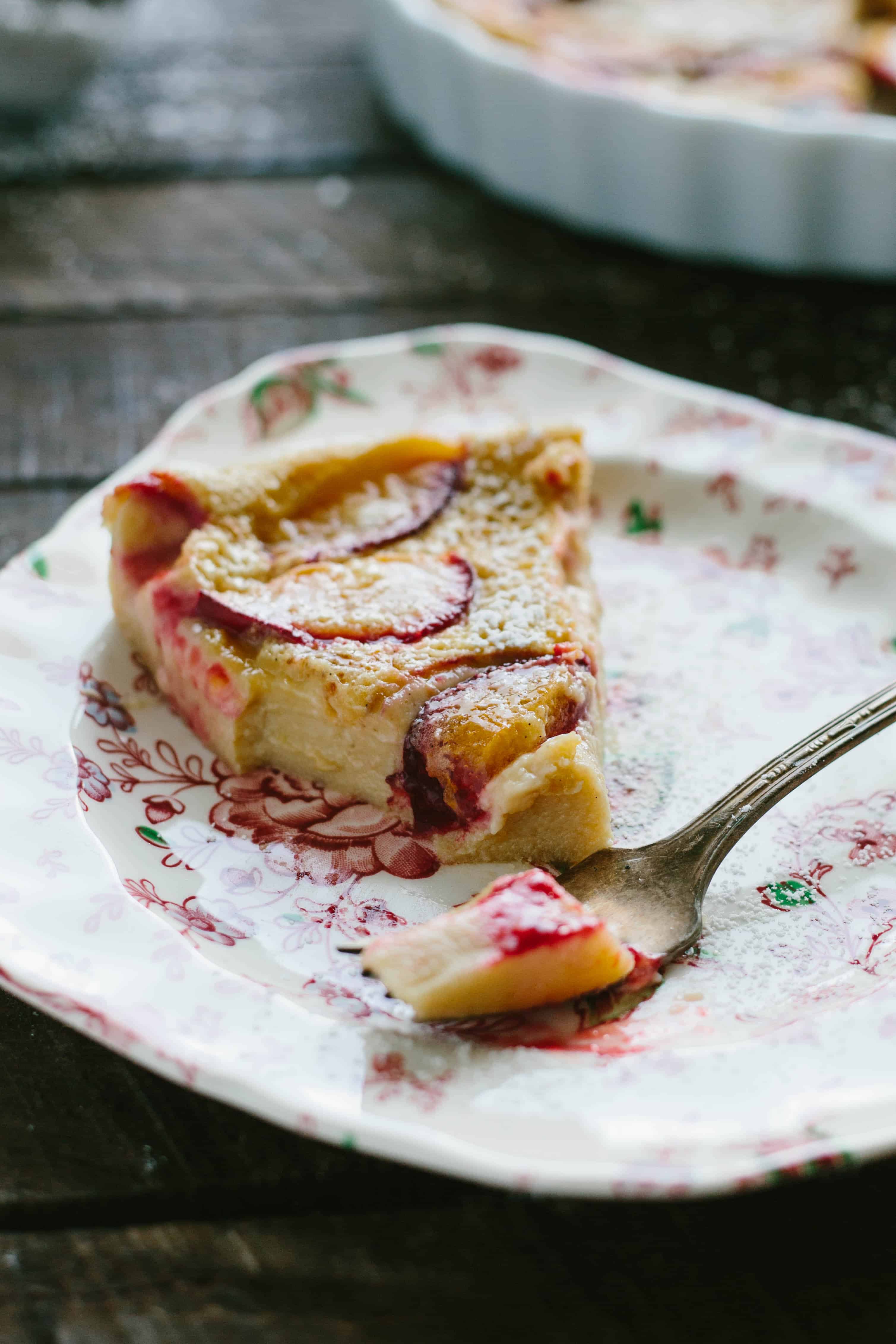 Triangle slice of plum clafoutis on a floral plate.