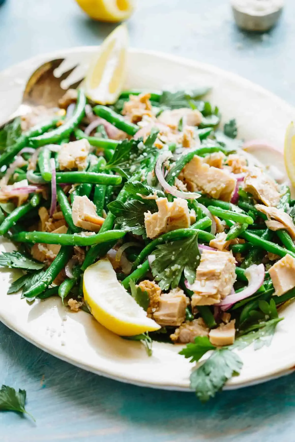 Close up of green bean salad with tuna and red onion plus lemon wedges.