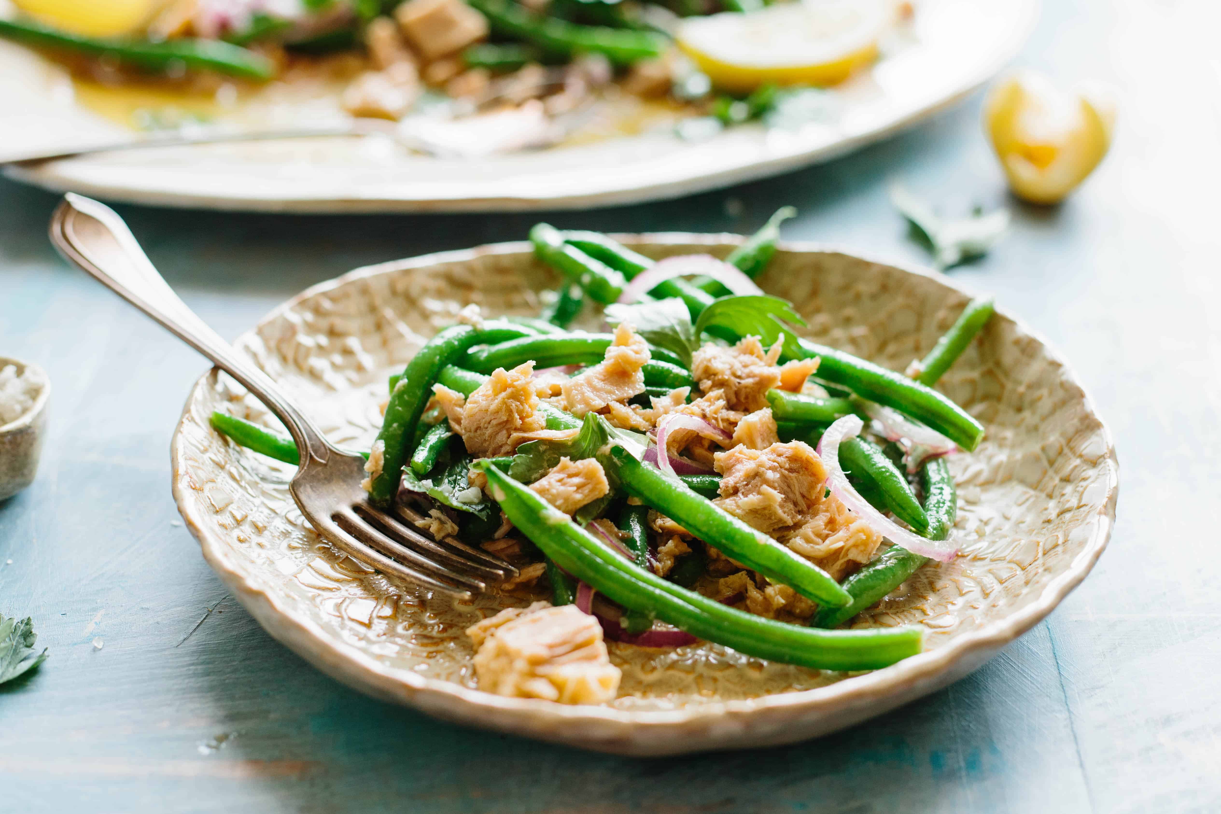 Small tan plate with a serving of green bean salad with tuna and onion.