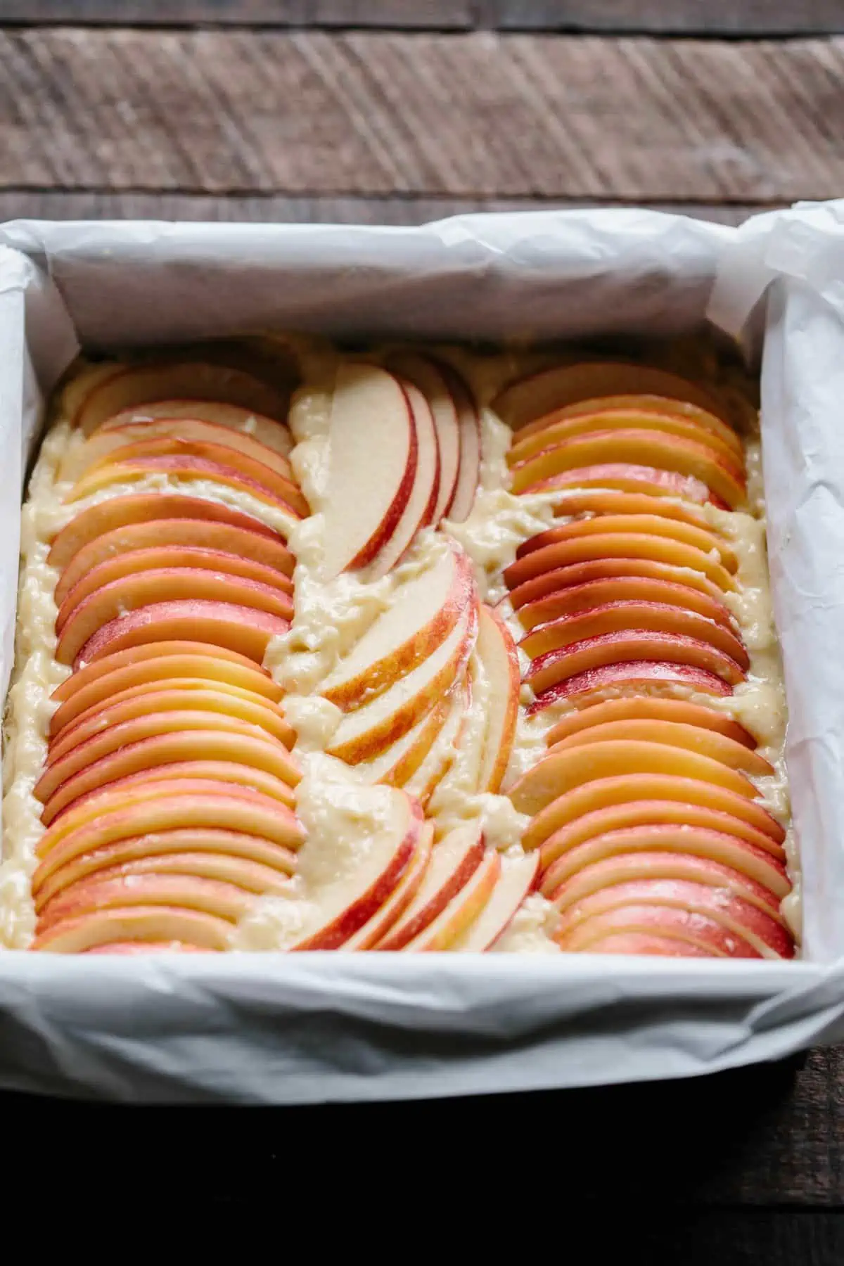 Thinly sliced apples lines up in a square baking pan of shortbread batter.