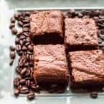 Espresso brownie squares on a tray surrounded by whole coffee beans.