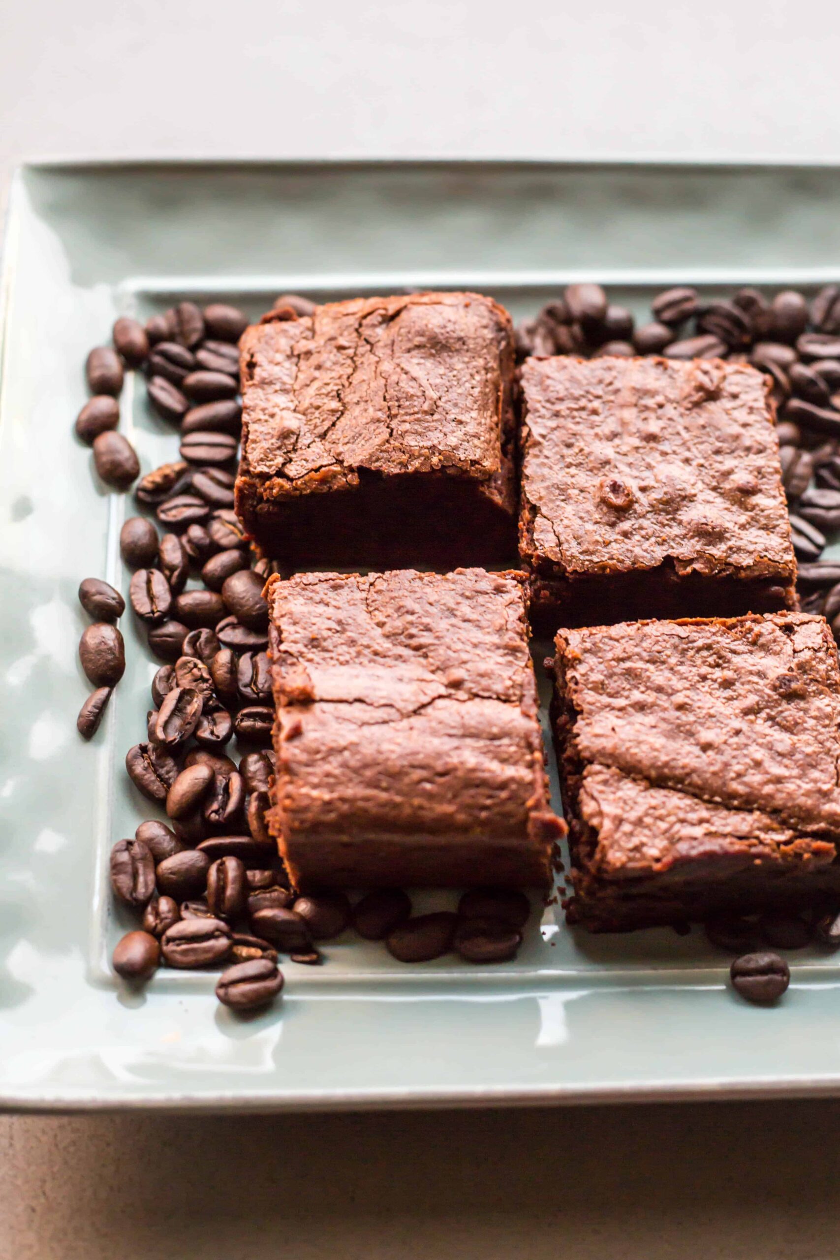 Espresso brownie squares on a tray surrounded by whole coffee beans.