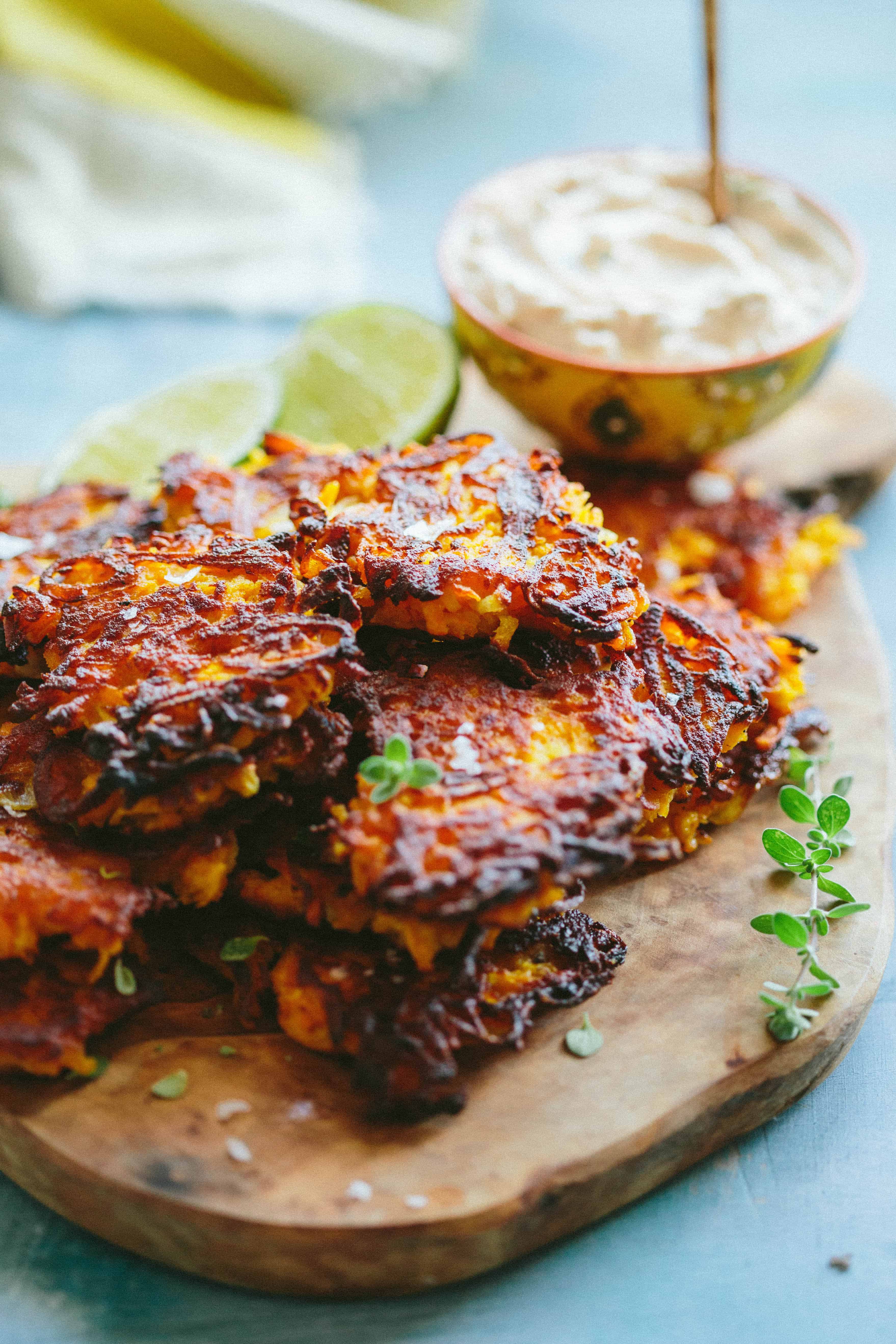 Butternut squash fritters on a wood platter next to sliced limes and a bowl of spiced yogurt.