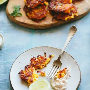 A plate with a fork and butternut squash fritters next to a wood serving platter.
